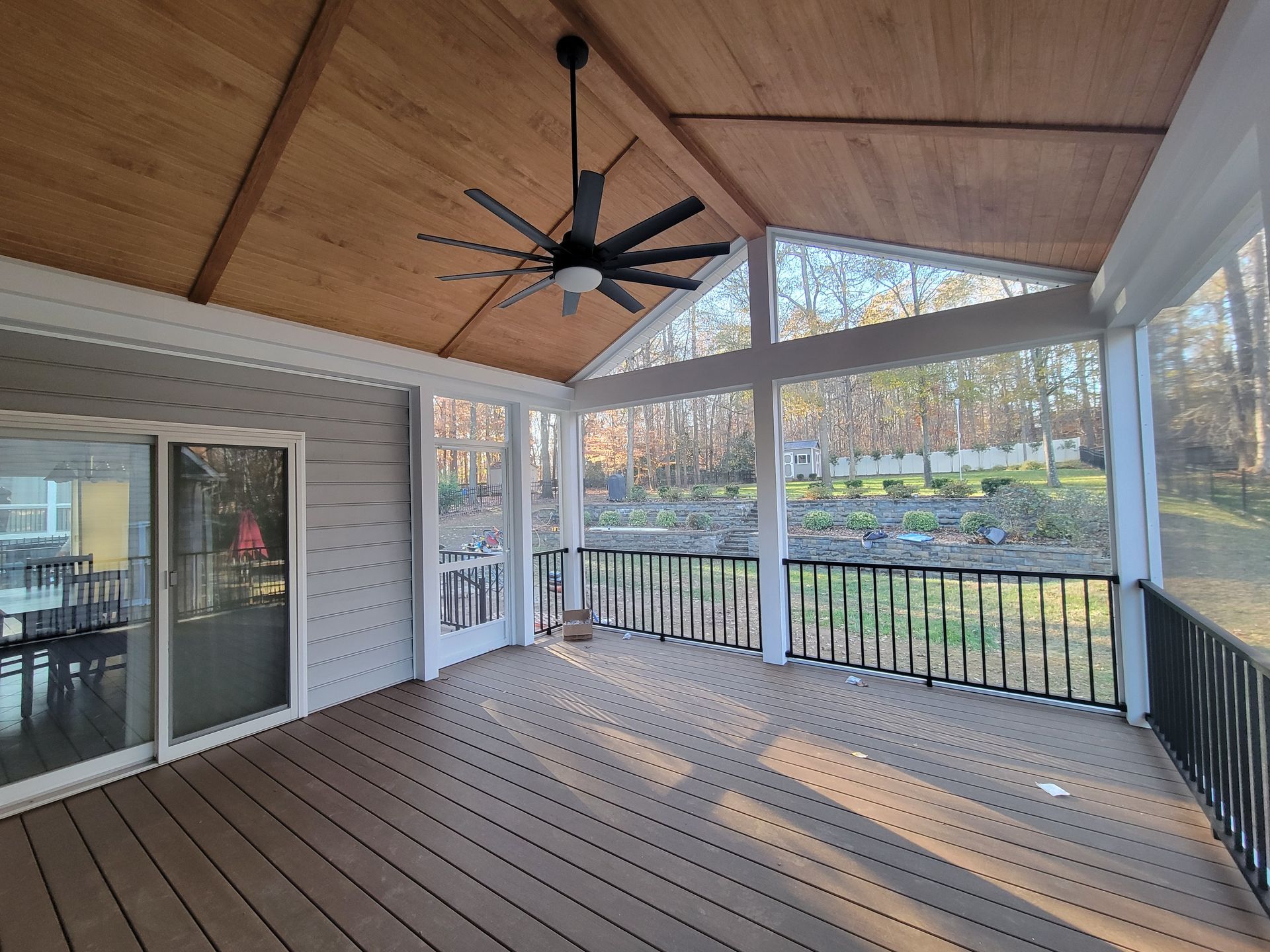 Covered wooden deck with ceiling fan, black railing, and sliding glass doors overlooking a yard