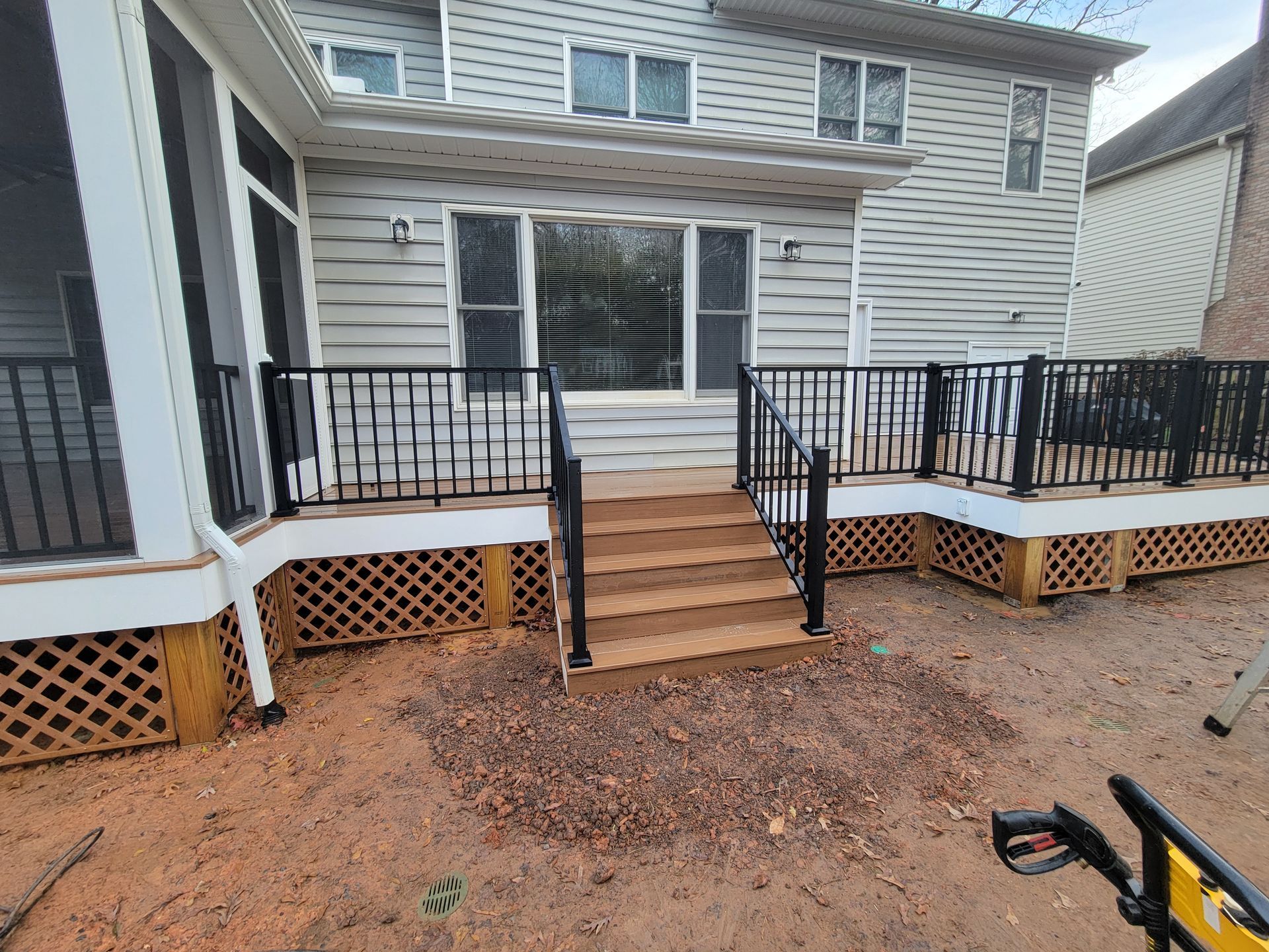 Backyard wooden deck with black railings and central steps leading to a house door