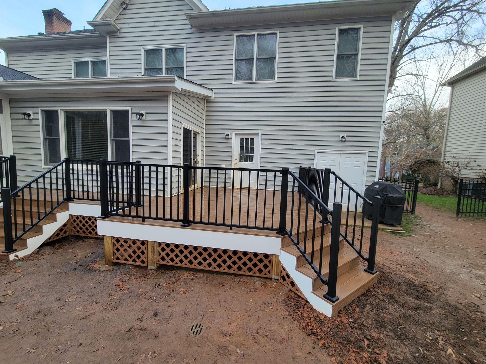 Rear house deck with black railings and white lattice skirting beside a beige siding home