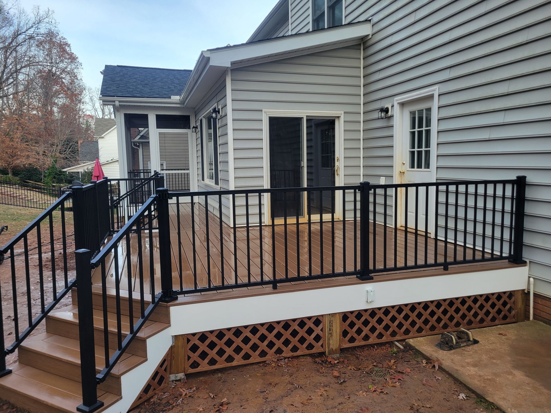 Back deck with black railings and wooden floor attached to a gray house with steps and lattice skirting