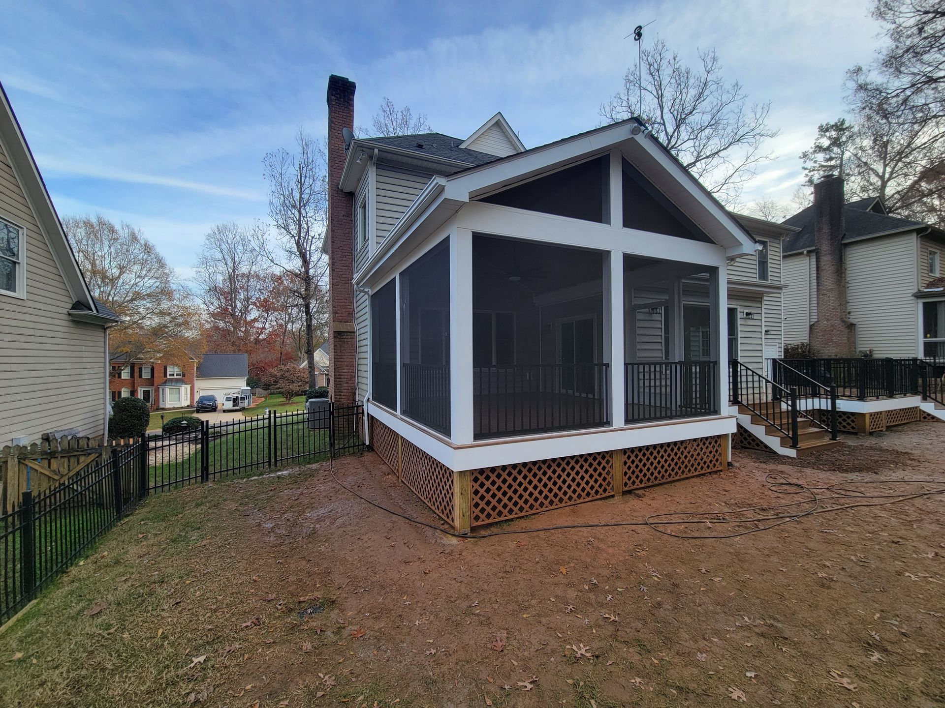 Small screened porch addition on a house with white trim and brick foundation in a wooded backyard.