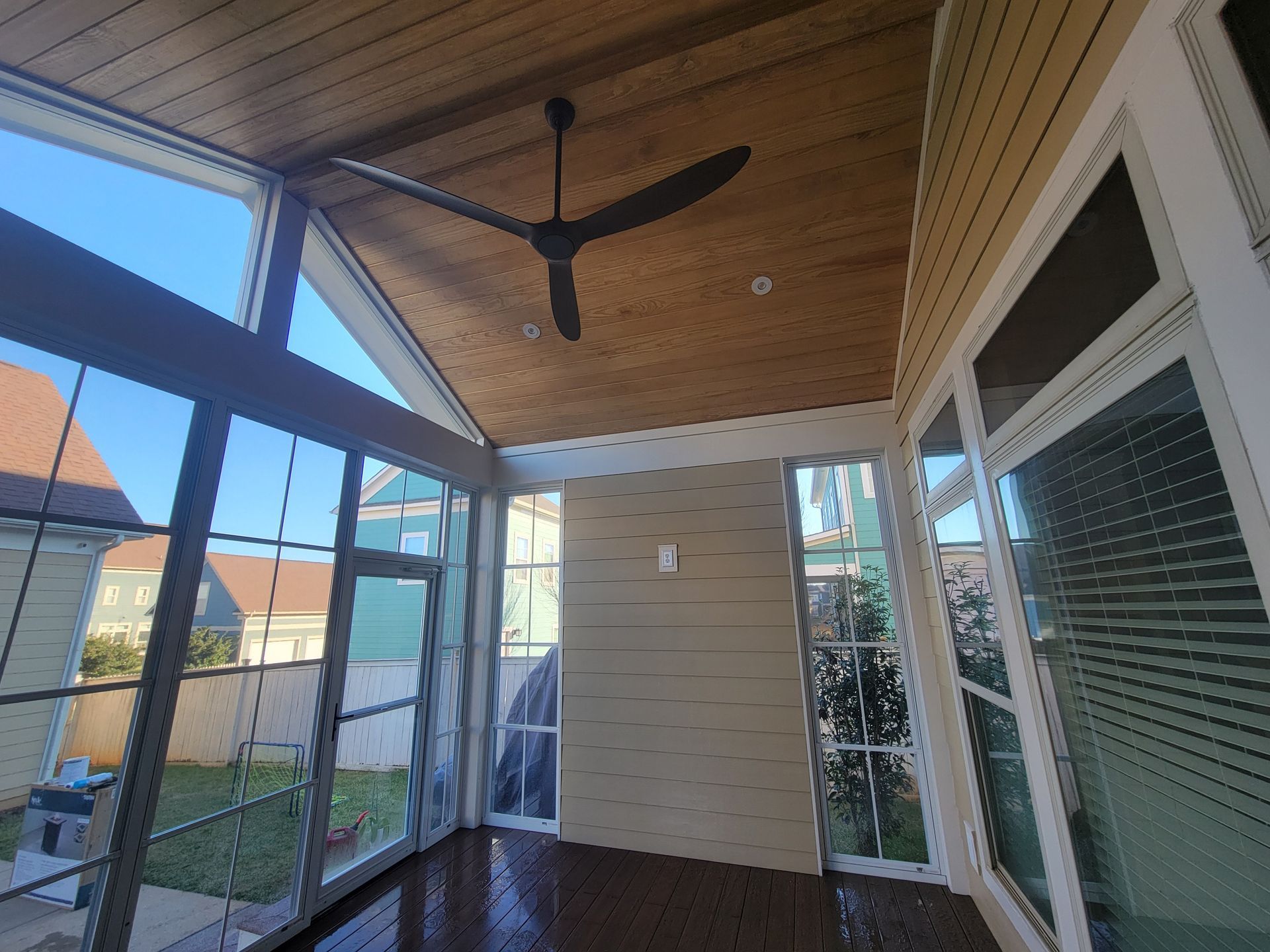 Covered patio with wood ceiling, black ceiling fan, screen panels, and house siding.