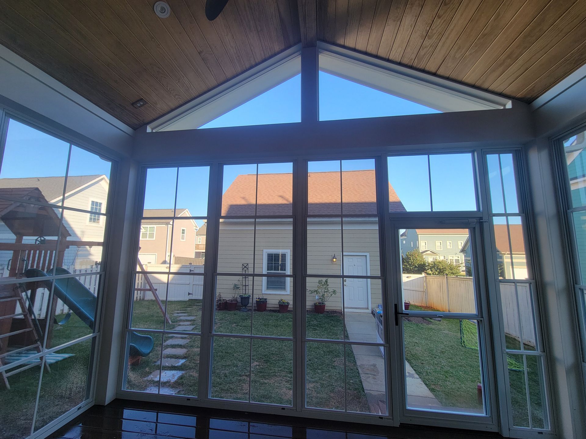 Sunroom interior with floor-to-ceiling windows facing a backyard and neighboring house.