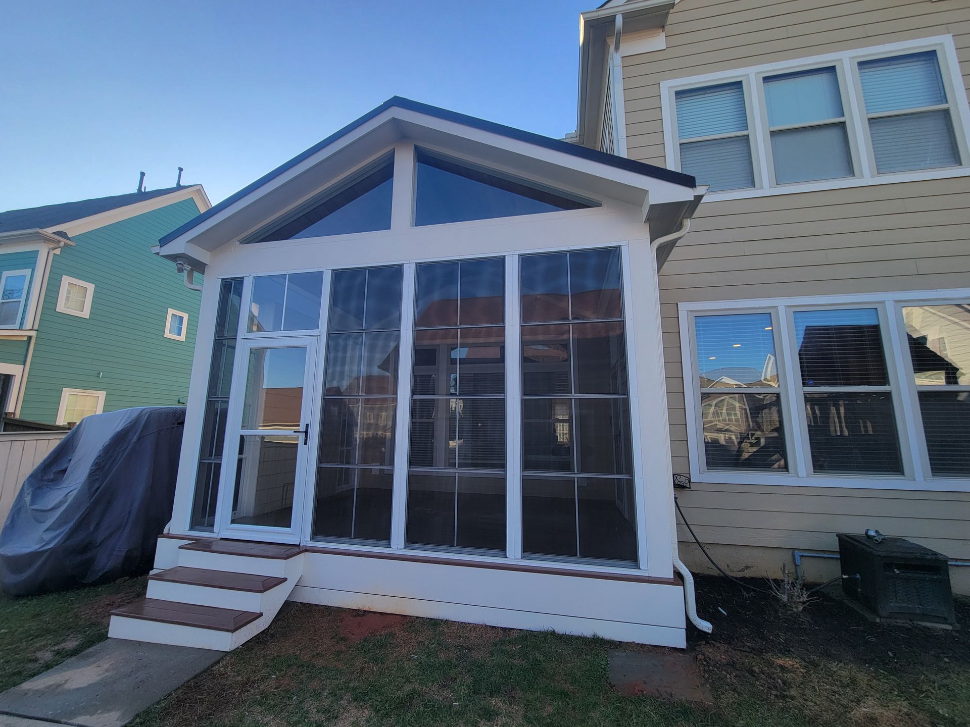 Small white sunroom addition with large windows attached to a beige house in a residential neighborhood