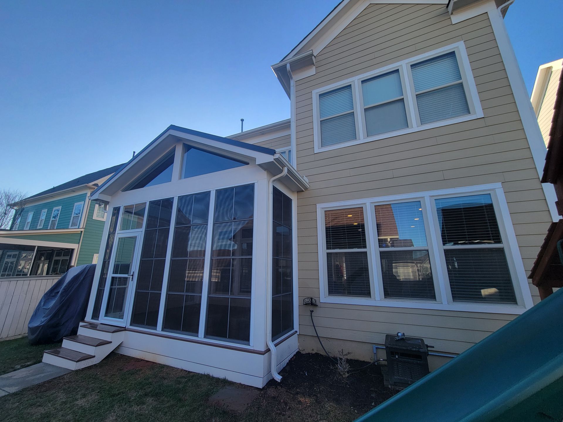 Backyard view of a beige two-story house with a sunroom and white-trimmed windows.