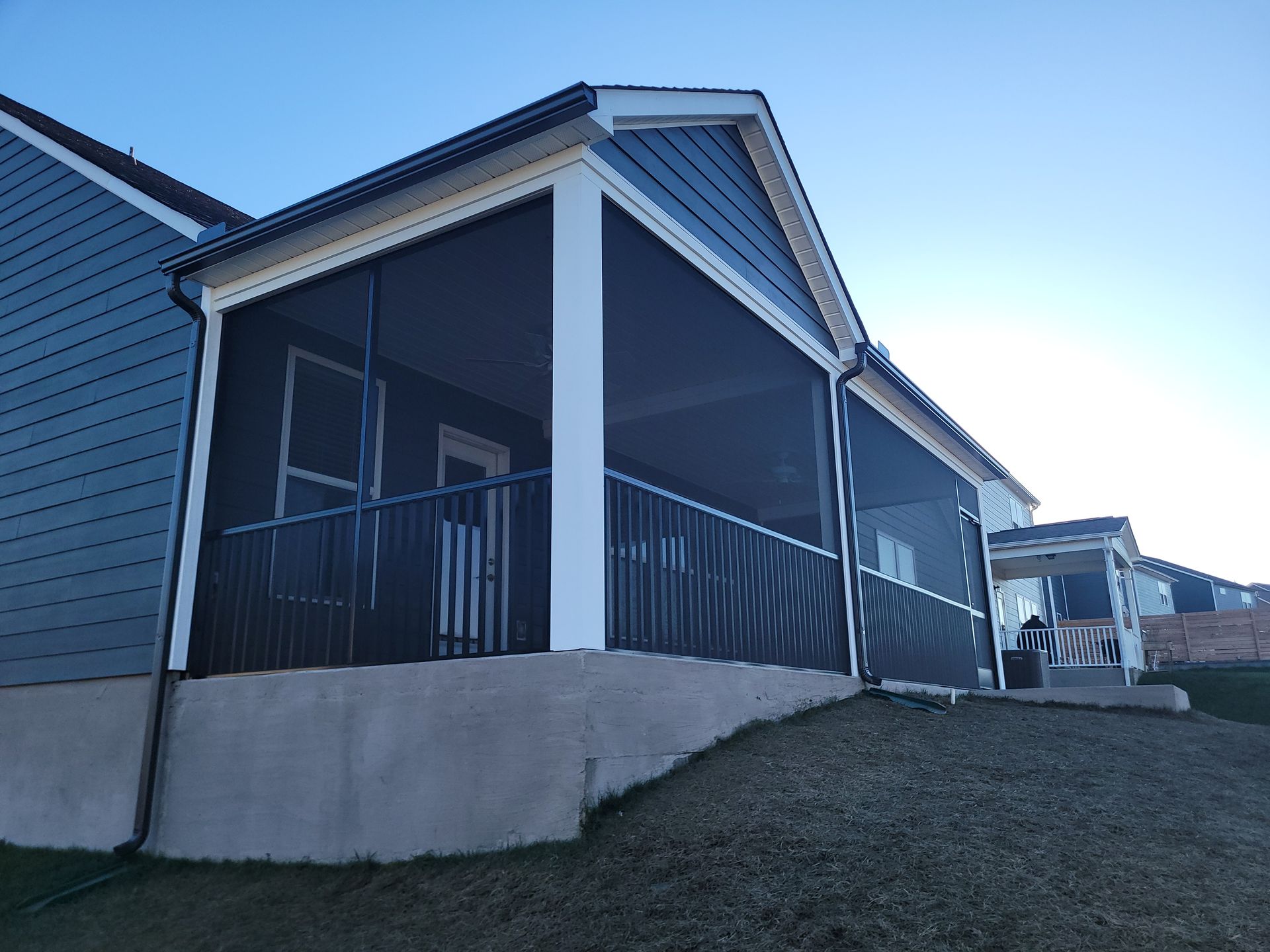 Covered porch with black railings on a gray house, viewed from a grassy yard.
