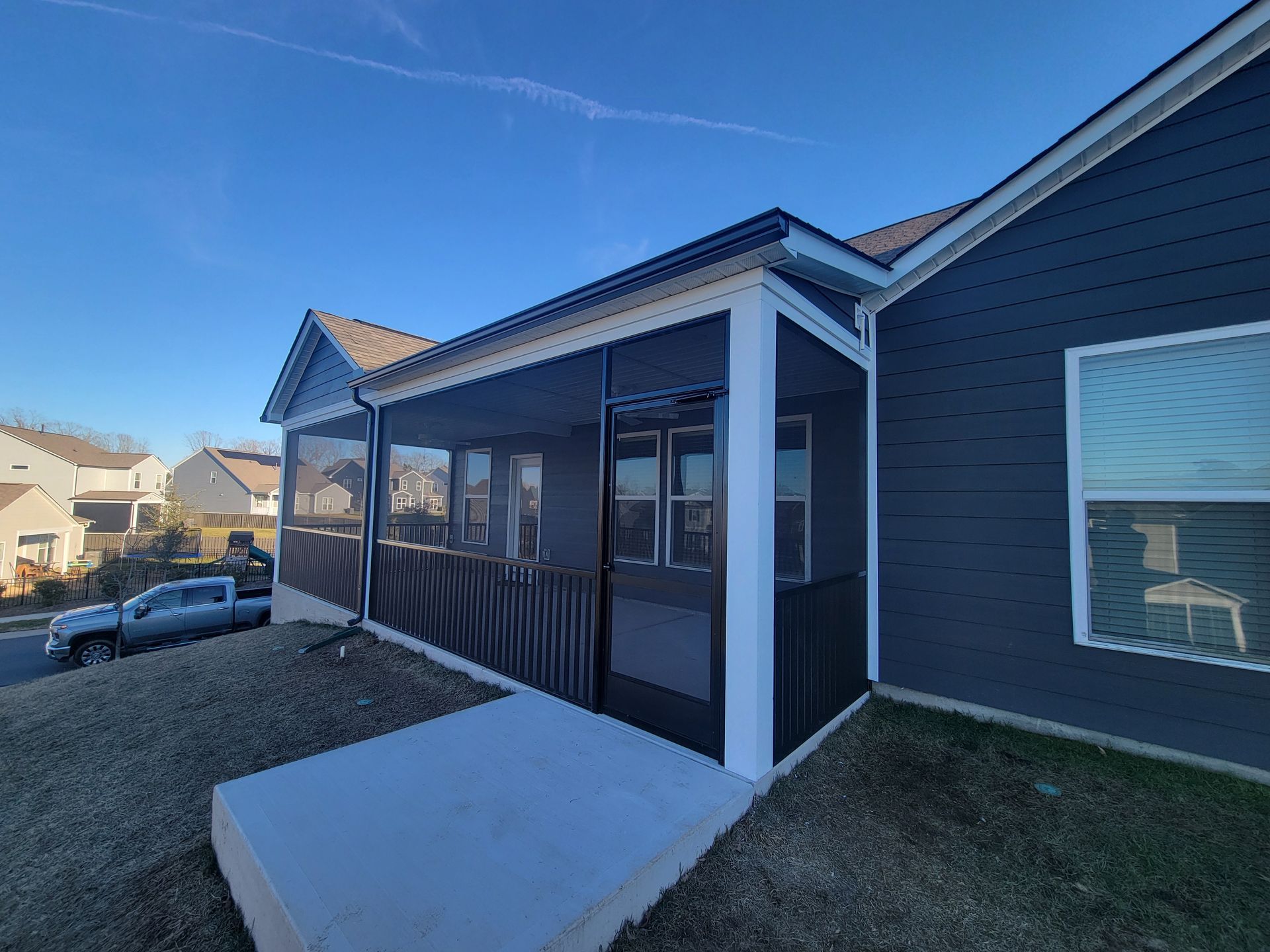 Front porch with screened entry and dark blue siding on a house, beside a gravel driveway.