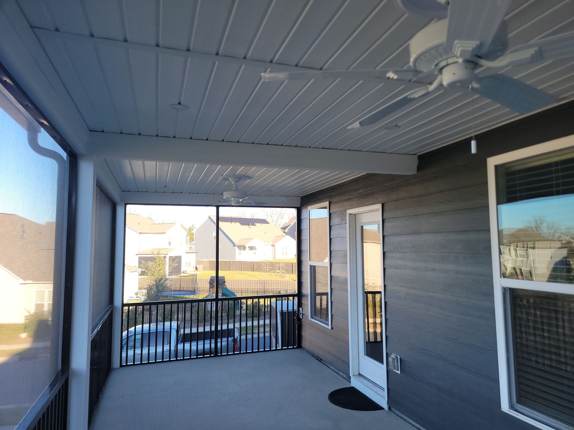 Covered porch with white ceiling fan, dark siding, and black railing overlooking parked cars.