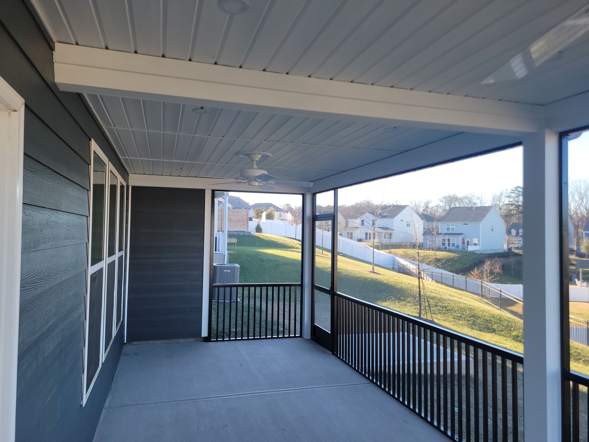 Covered front porch with gray siding, black railing, and a view of a grassy neighborhood street.