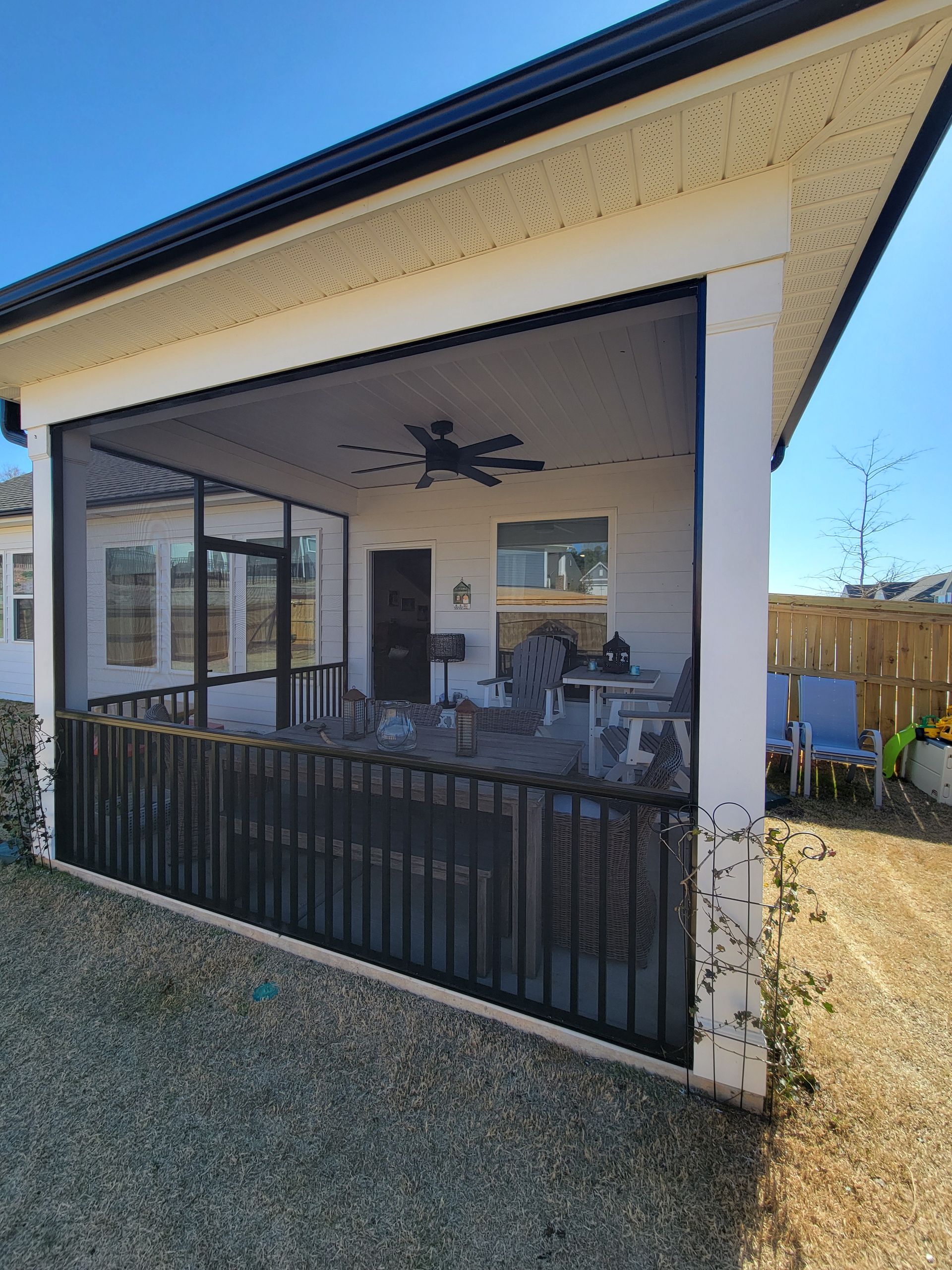 Covered backyard patio with black railings, outdoor seating, and ceiling fan beside a house