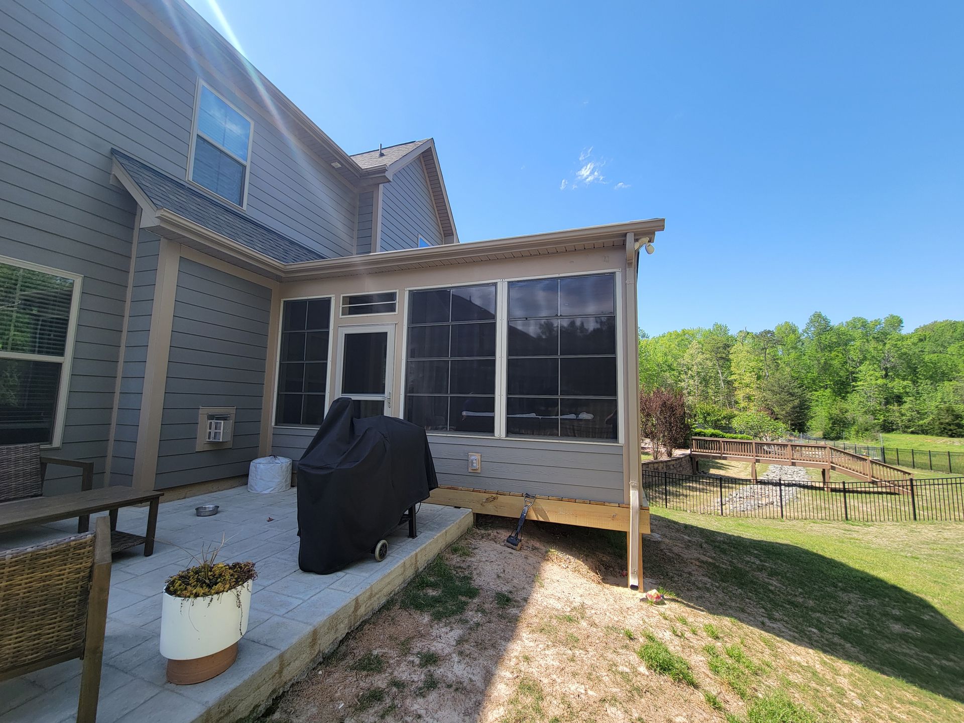 Back patio with screened porch, black grill, white planter, and grassy yard under a blue sky