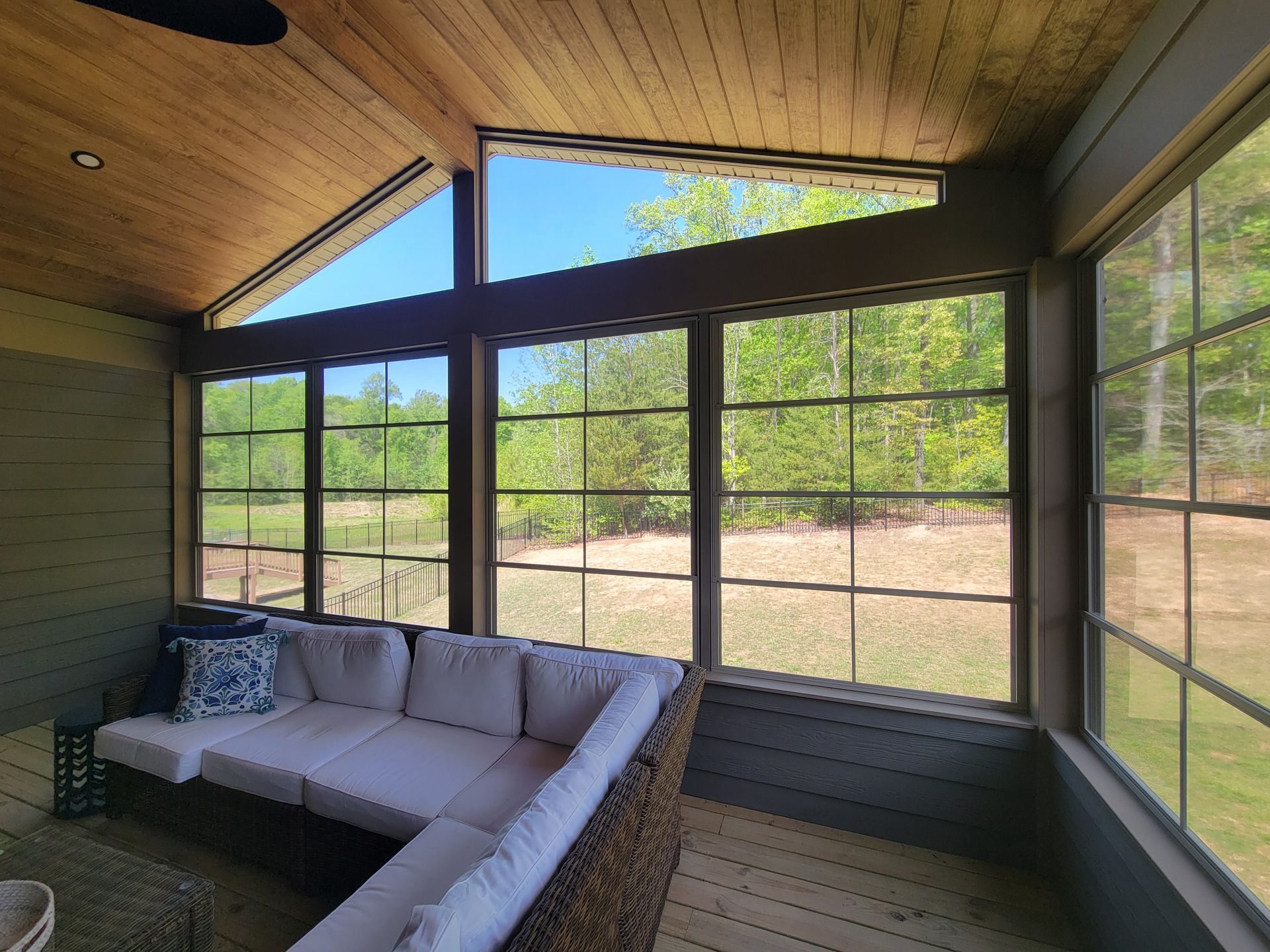 Sunroom with large windows, wood ceiling, and an L-shaped gray sectional sofa.