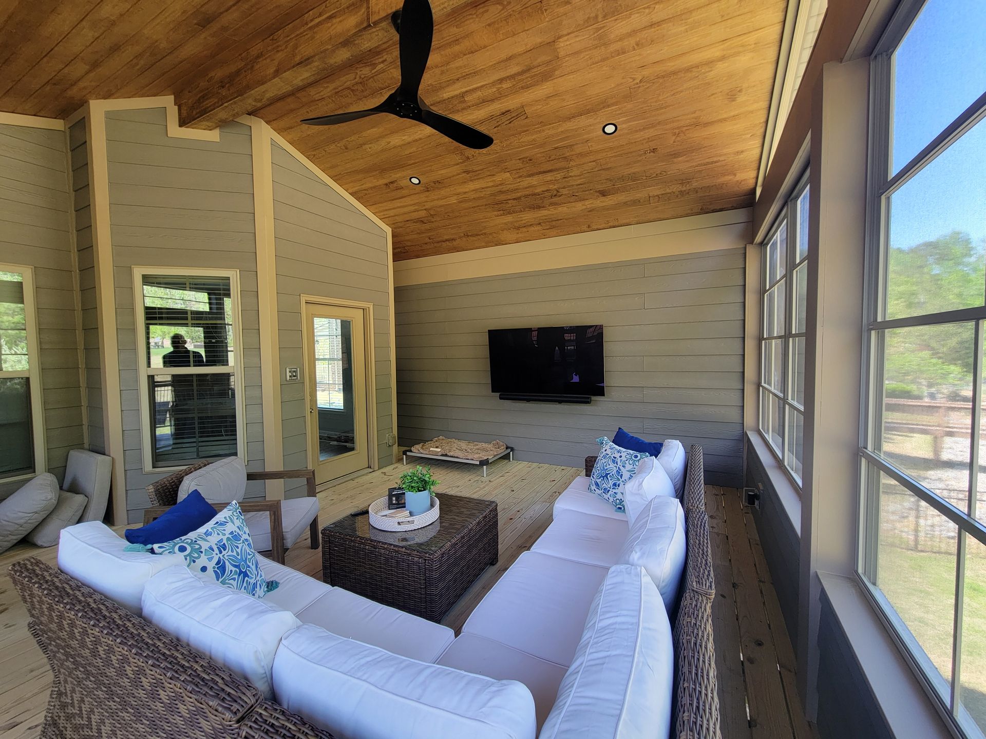 Modern living room with curved white sofa, wall-mounted TV, wood ceiling, and large windows