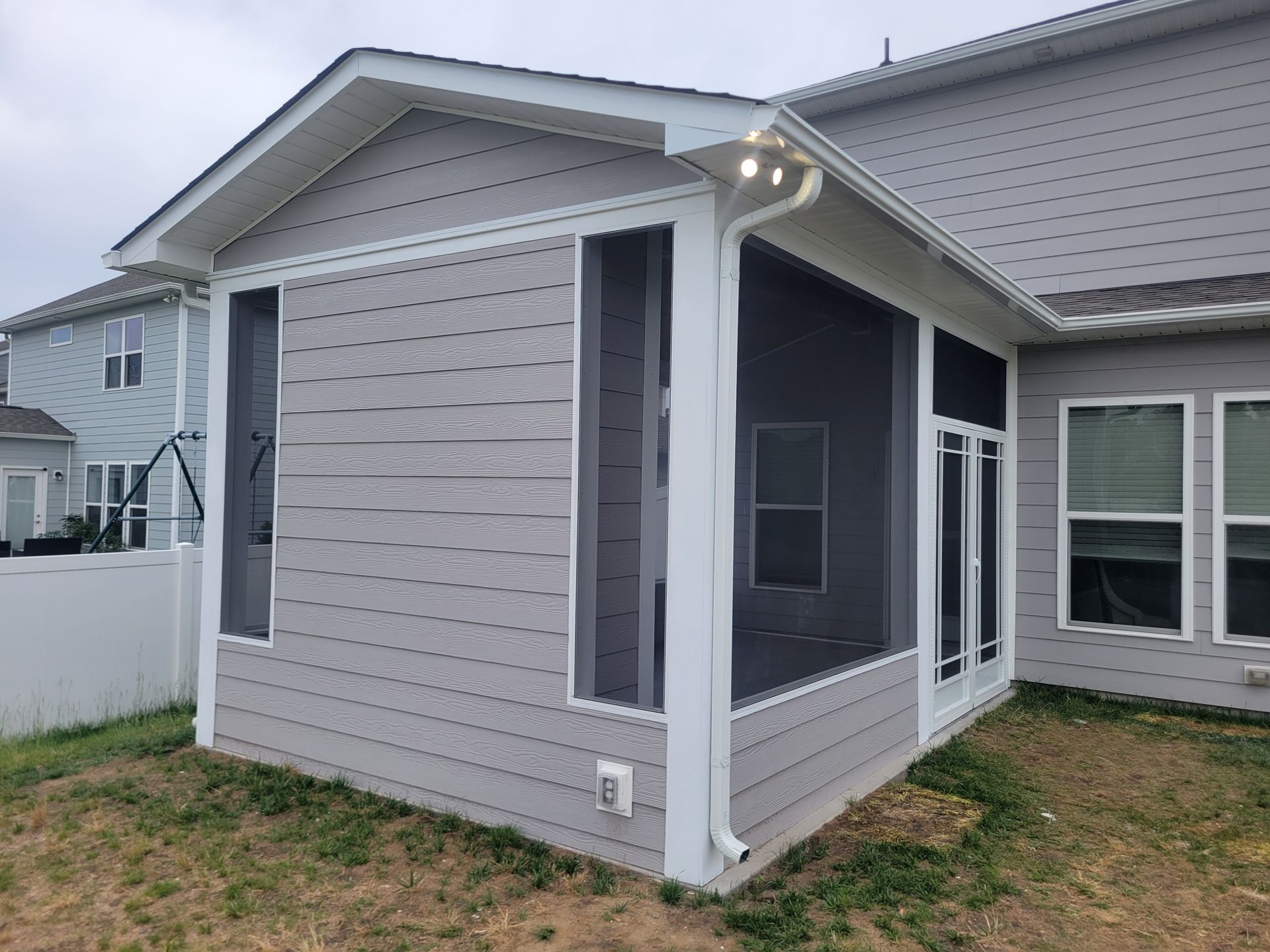 Small screened porch attached to a gray house with white trim and sliding windows.