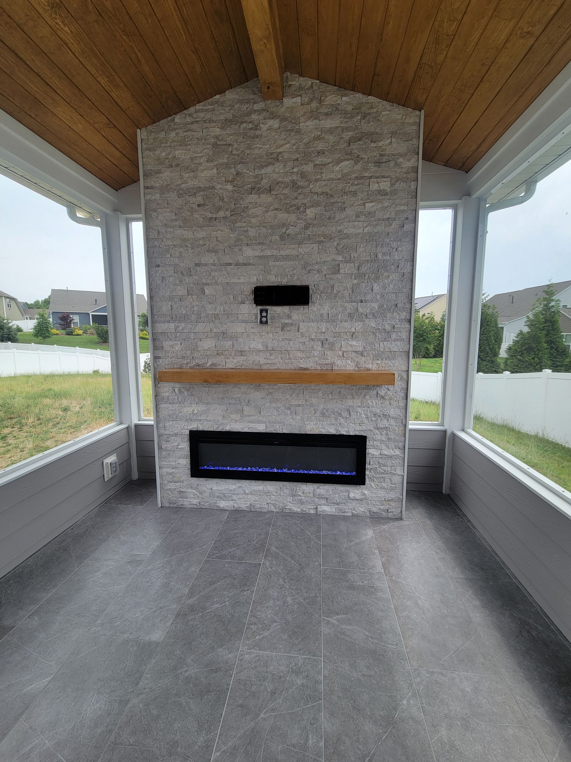 Covered outdoor fireplace with stone facing and wood ceiling in a screened patio.