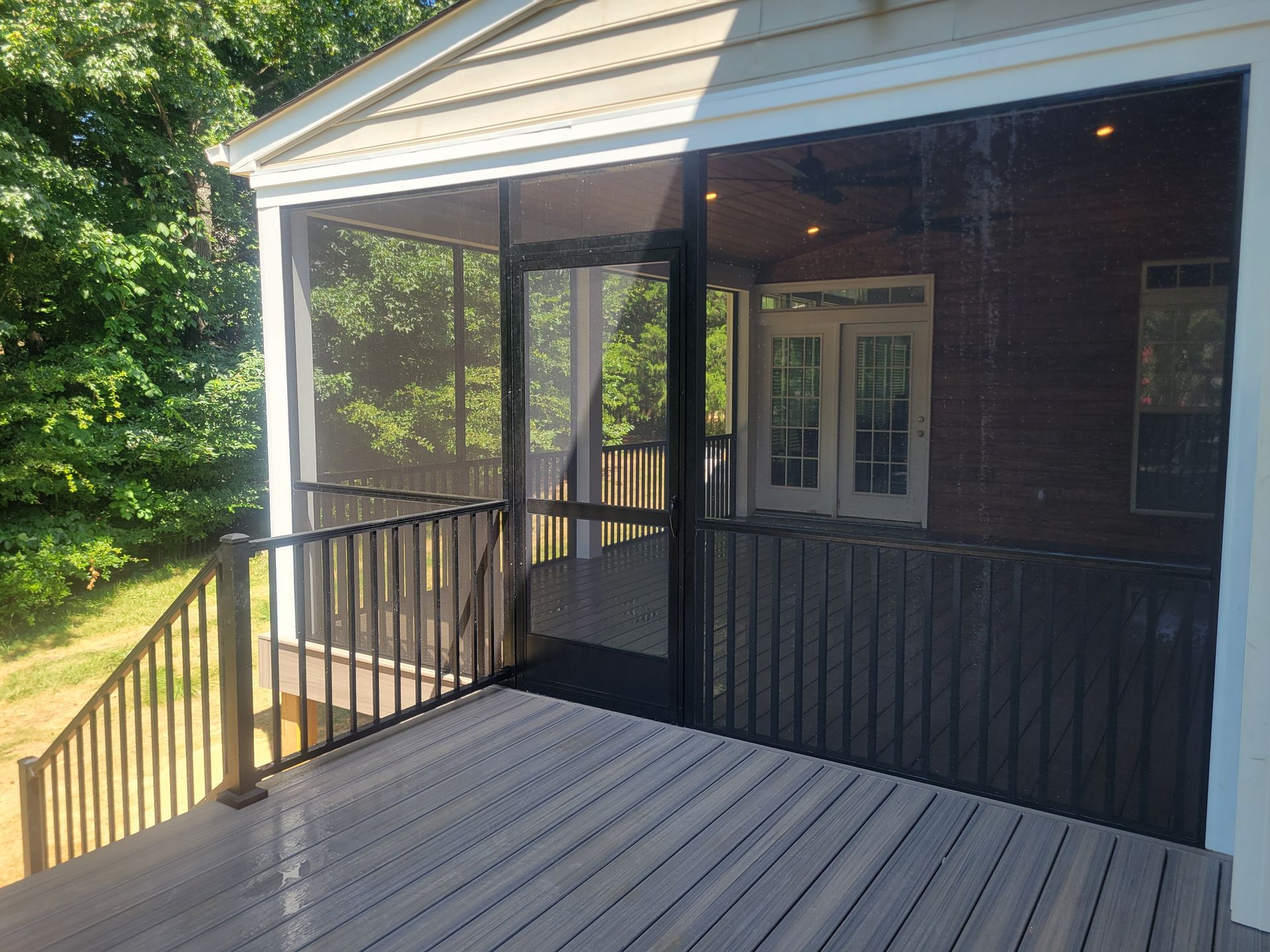 Covered porch with black railings, gray floorboards, and white columns on a brick house.