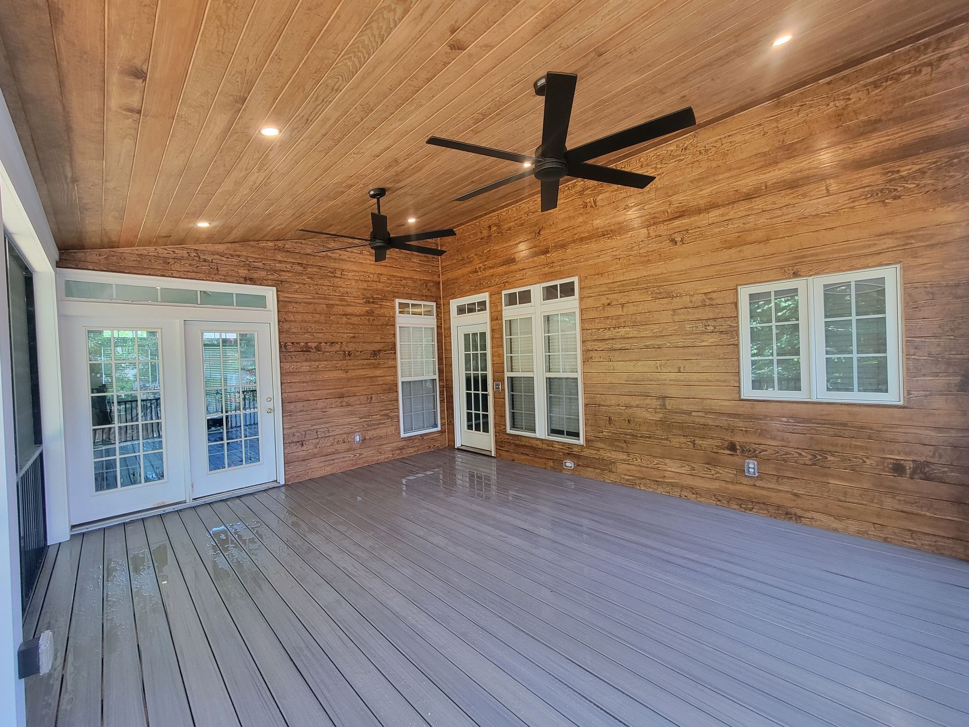 Covered wooden porch with ceiling fans, French doors, and windows overlooking the yard