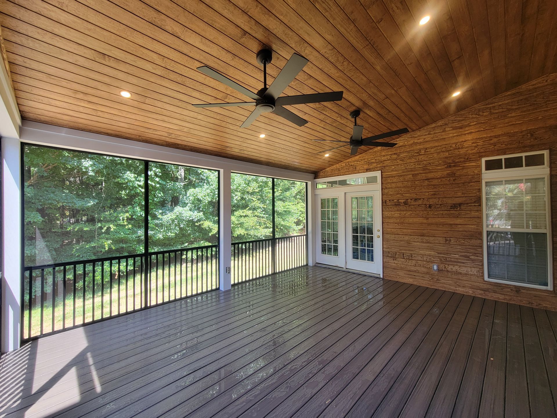 Covered screened porch with wood ceiling, ceiling fan, brick wall, and views of trees through large openings