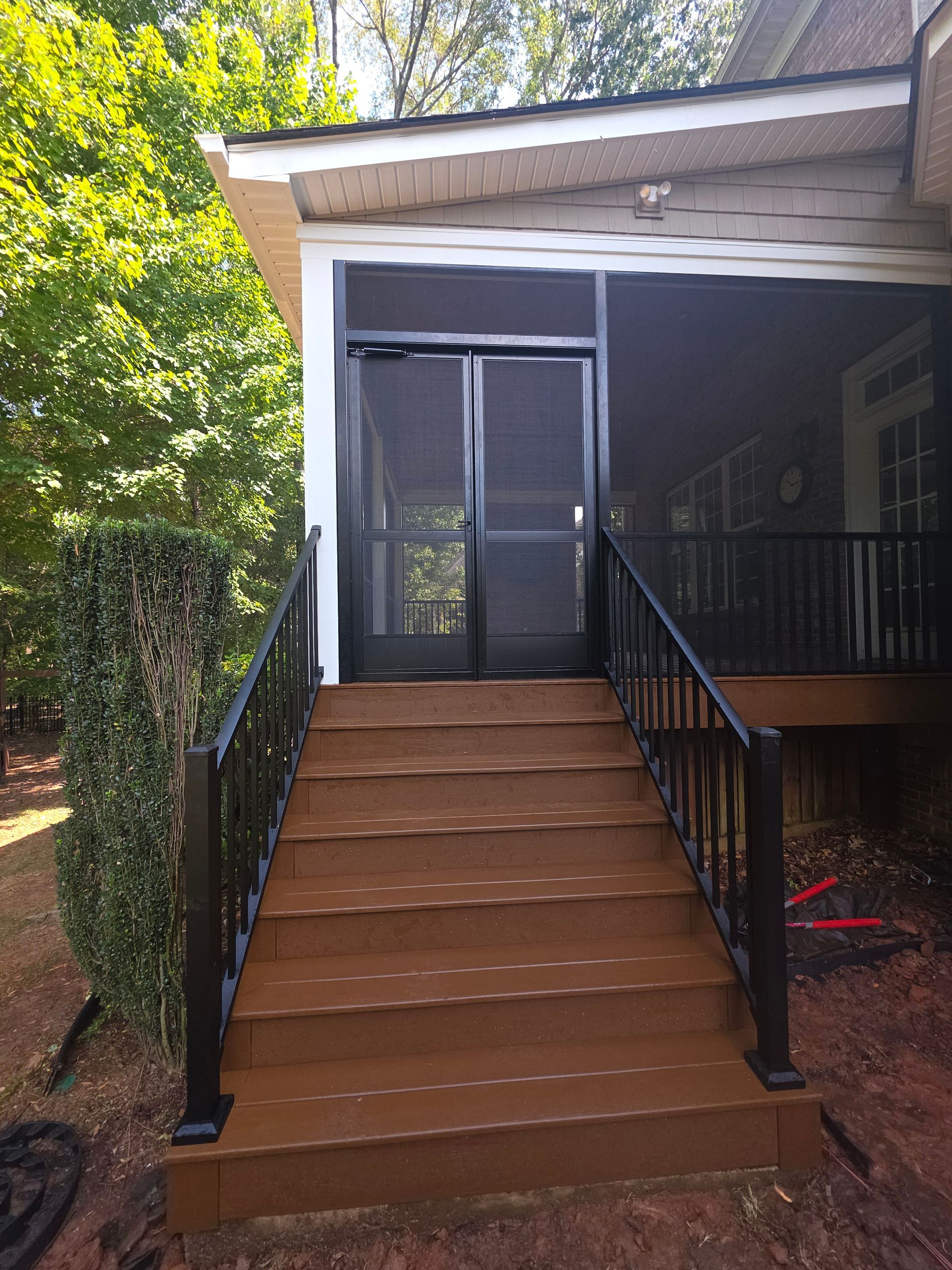 Front porch with brown stairs, black railings, and screened double doors under a white roof.