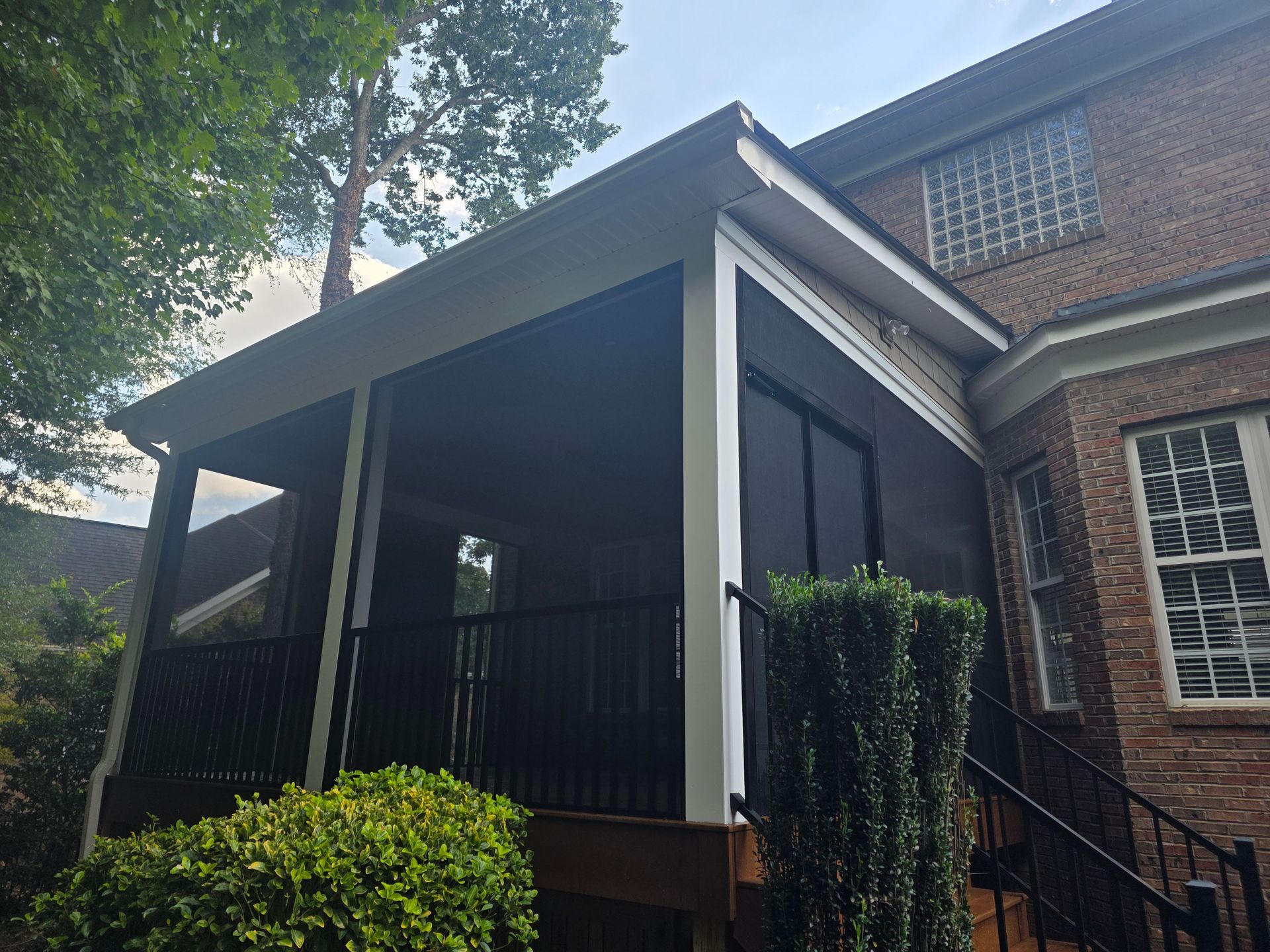 Brick house porch with white columns, black railings, and trimmed shrubs in front.