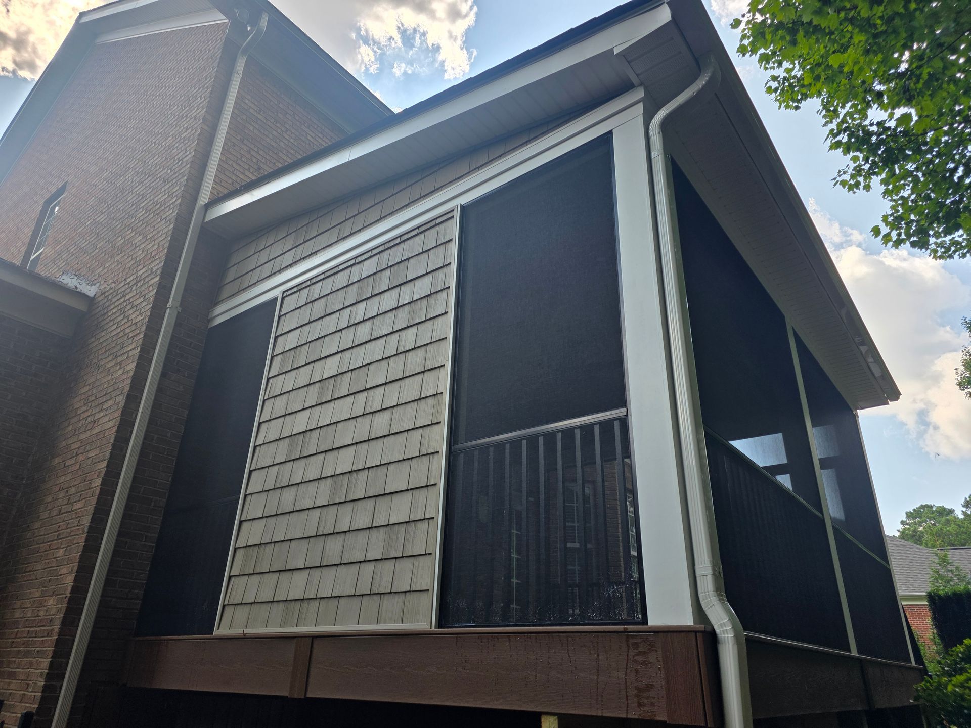 Exterior of a two-story house with gray siding, a screened porch, and brick walls under a partly cloudy sky