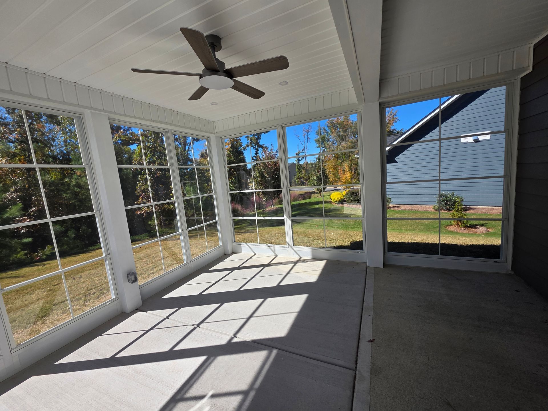 Enclosed screened porch with white ceiling, ceiling fan, and sunlight casting window shadows on the floor.