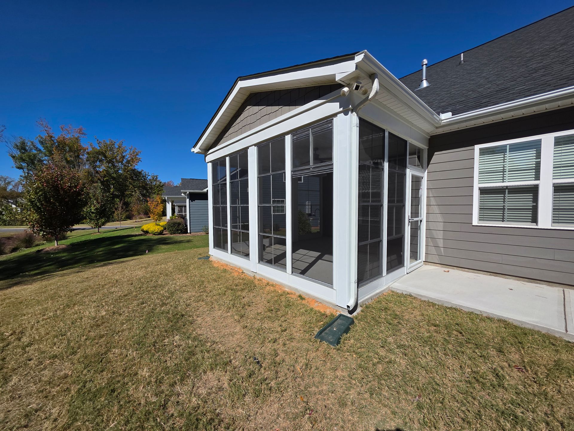 Screened porch on a house with white trim and gray siding, beside a grassy yard under a clear blue sky