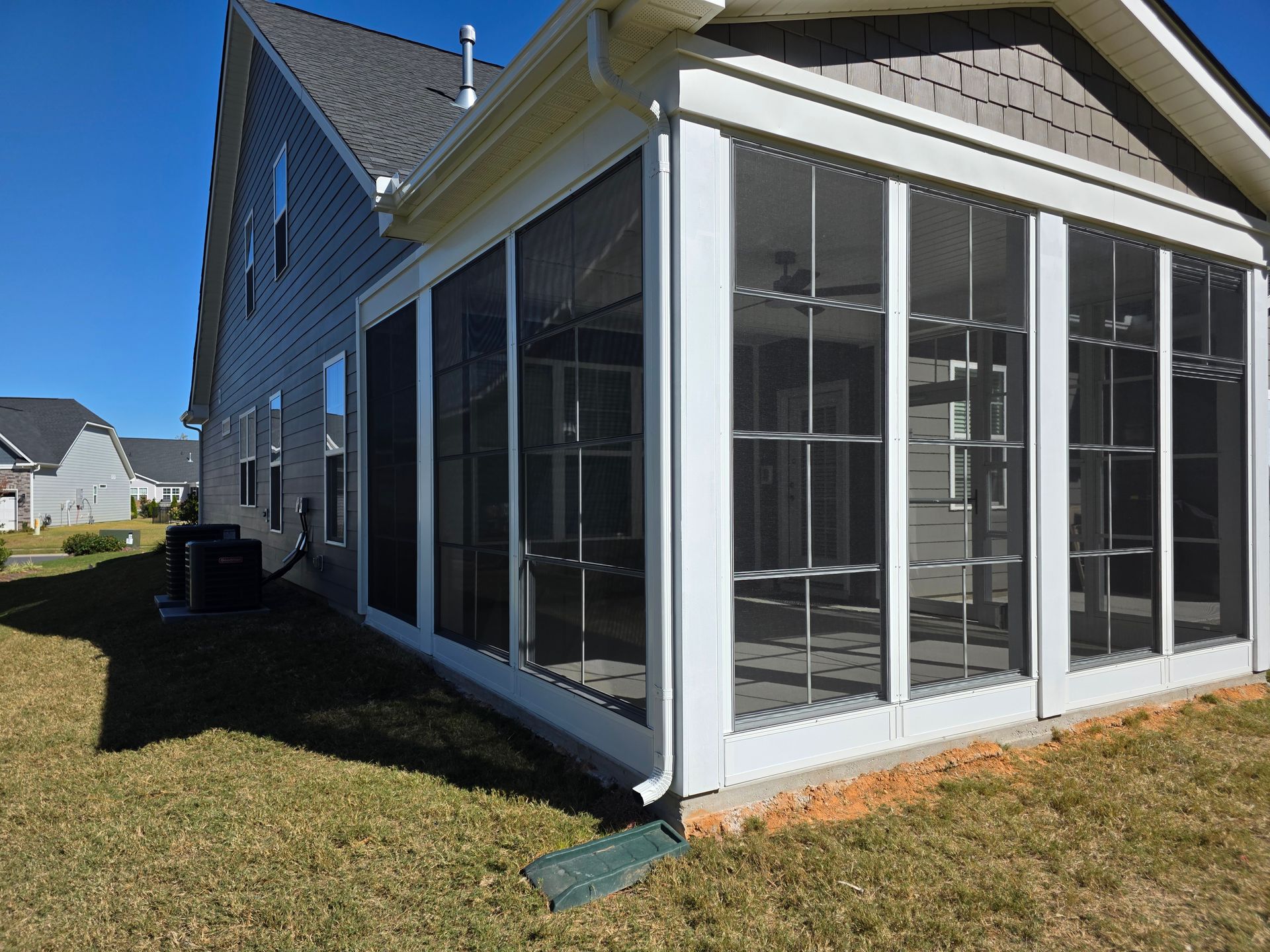 White screened porch attached to a beige house on a sunny lawn