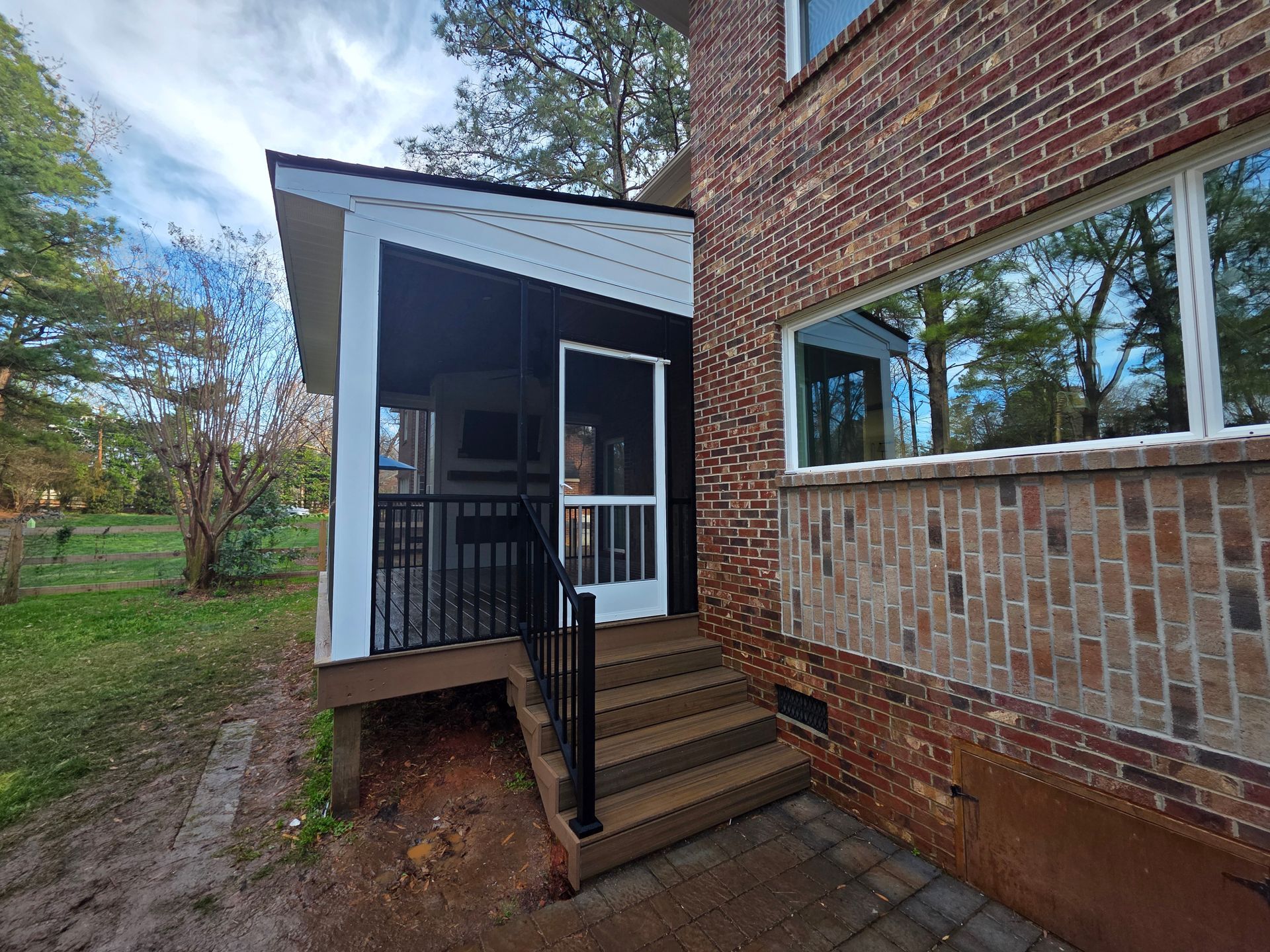 Brick house porch with steps, black railing, and white trim beside a grassy yard