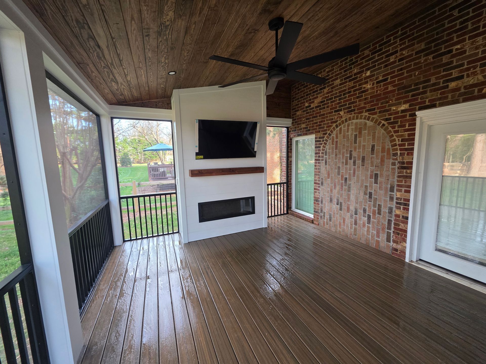 Covered porch with wood ceiling, brick wall, mounted TV, fireplace, and outdoor ceiling fan