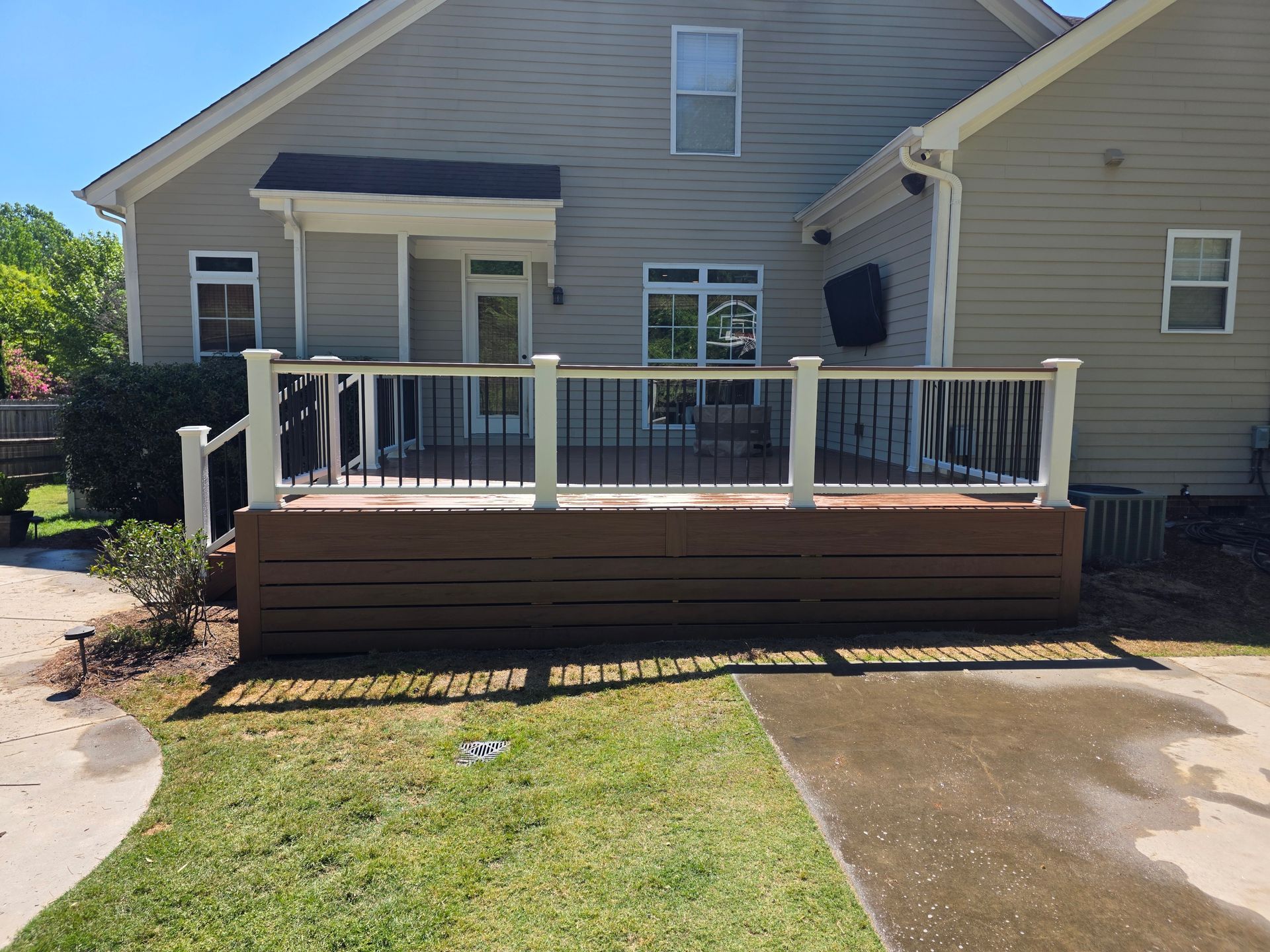 Front of a beige house with a wooden porch deck, white railings, and a concrete driveway.