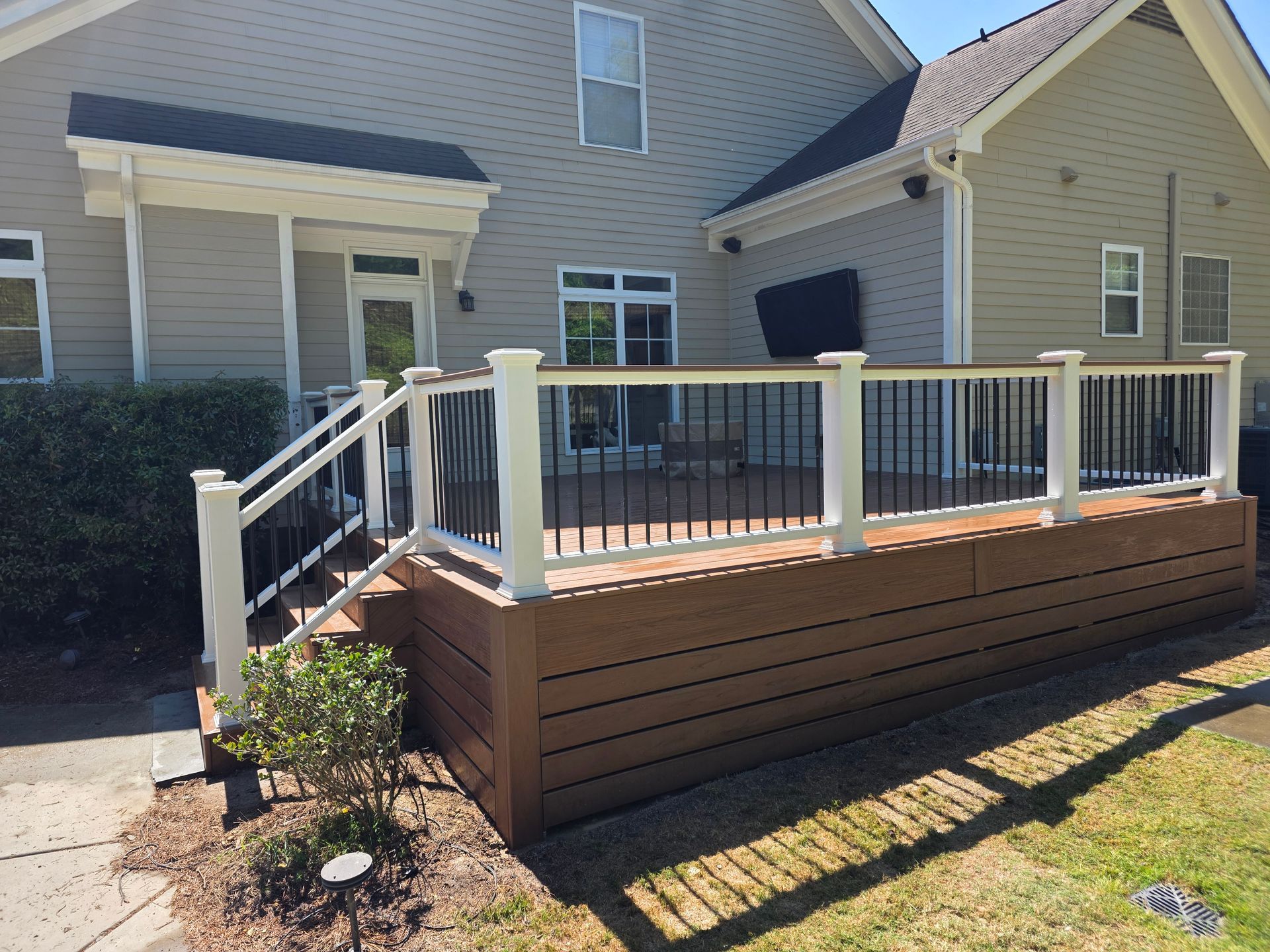 Backyard deck with white railings, brown skirting, and stairs beside a beige house