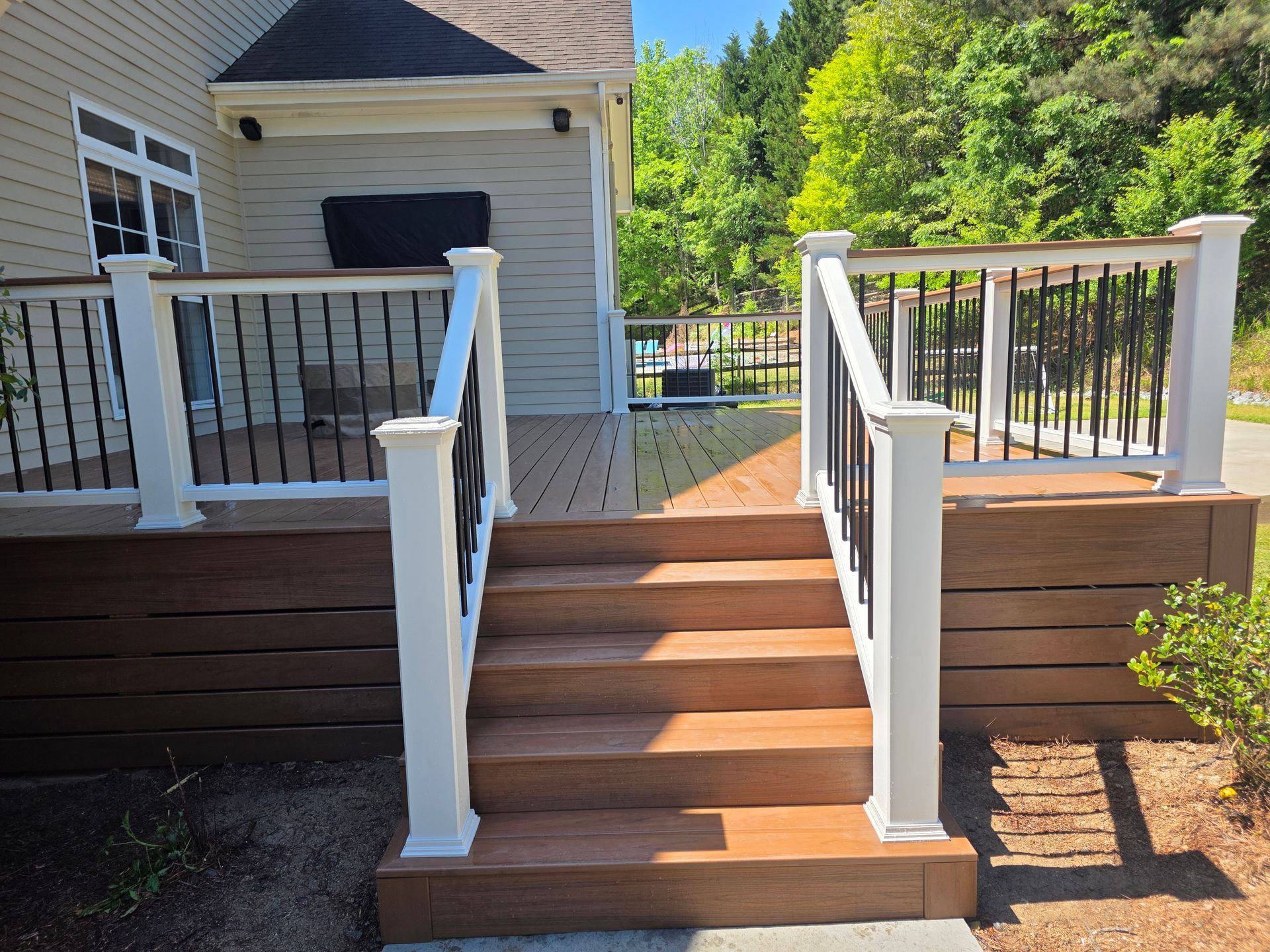 Front steps with white railings leading to a house deck, surrounded by greenery.