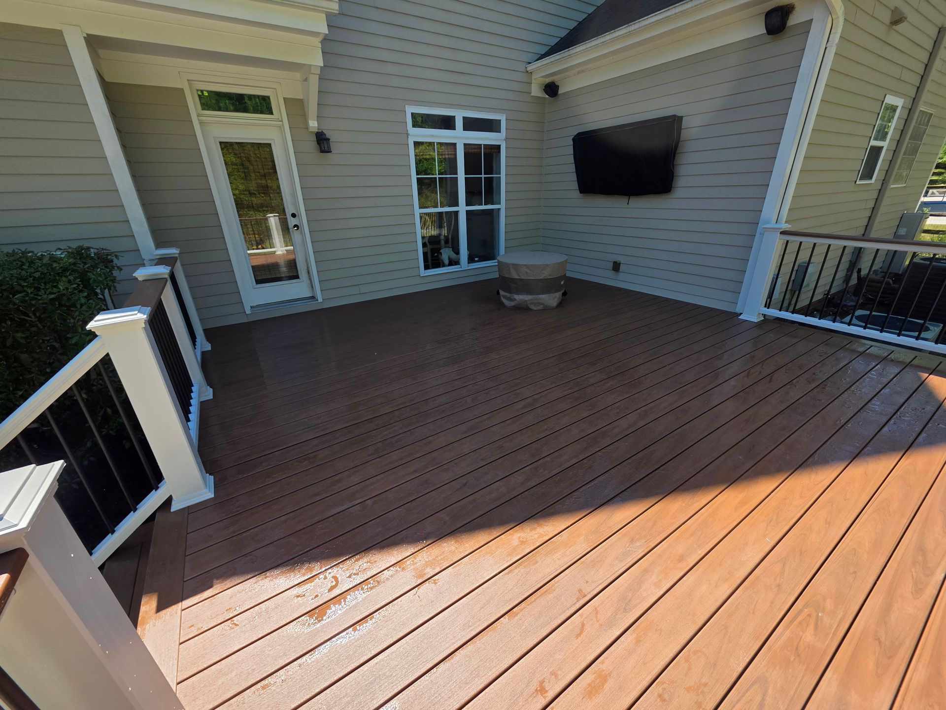 Wooden deck patio beside a beige house with white railing, French door, and window.