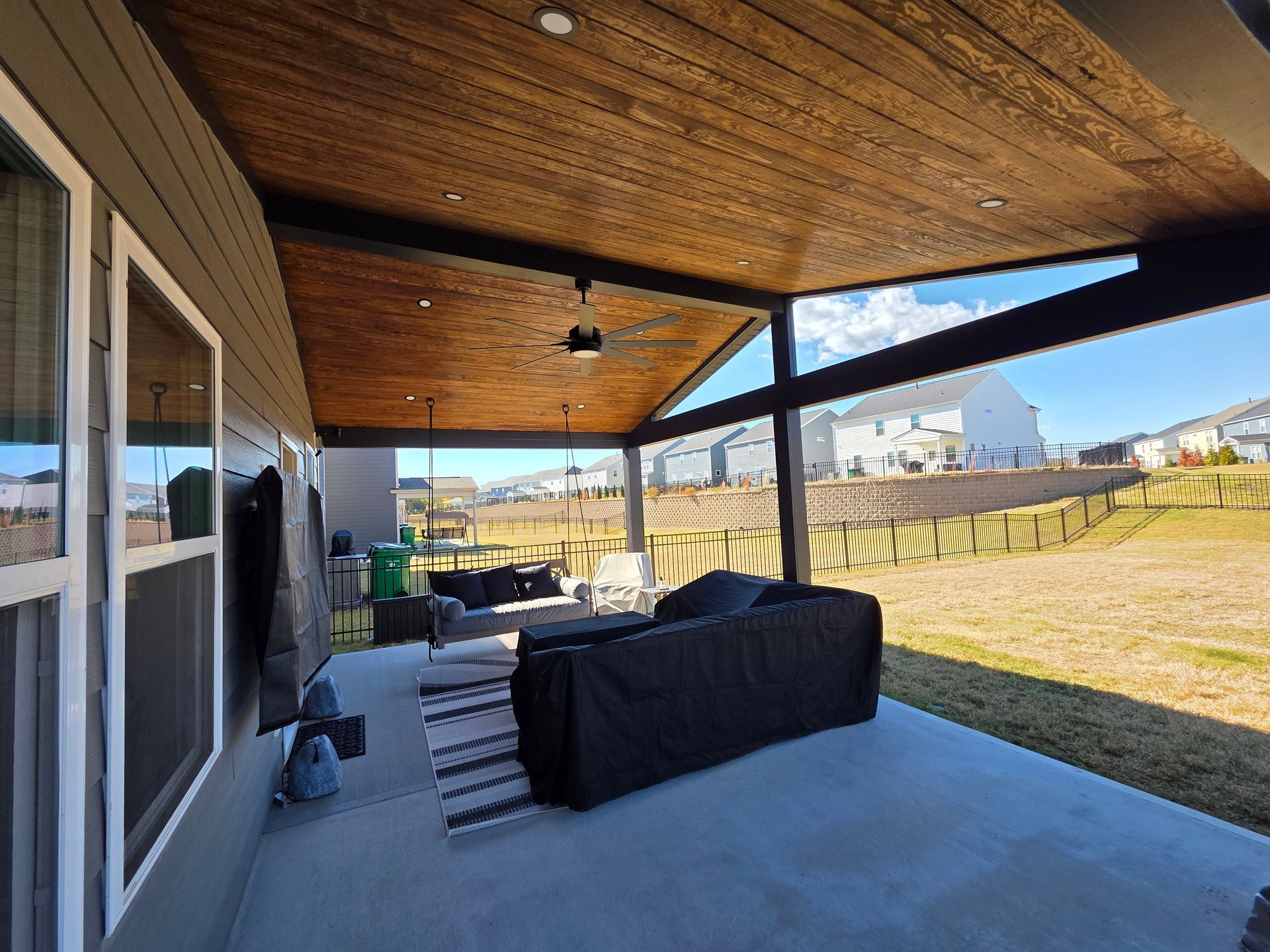 Covered patio with black sofa, wood ceiling, and view of a grassy yard and distant water.