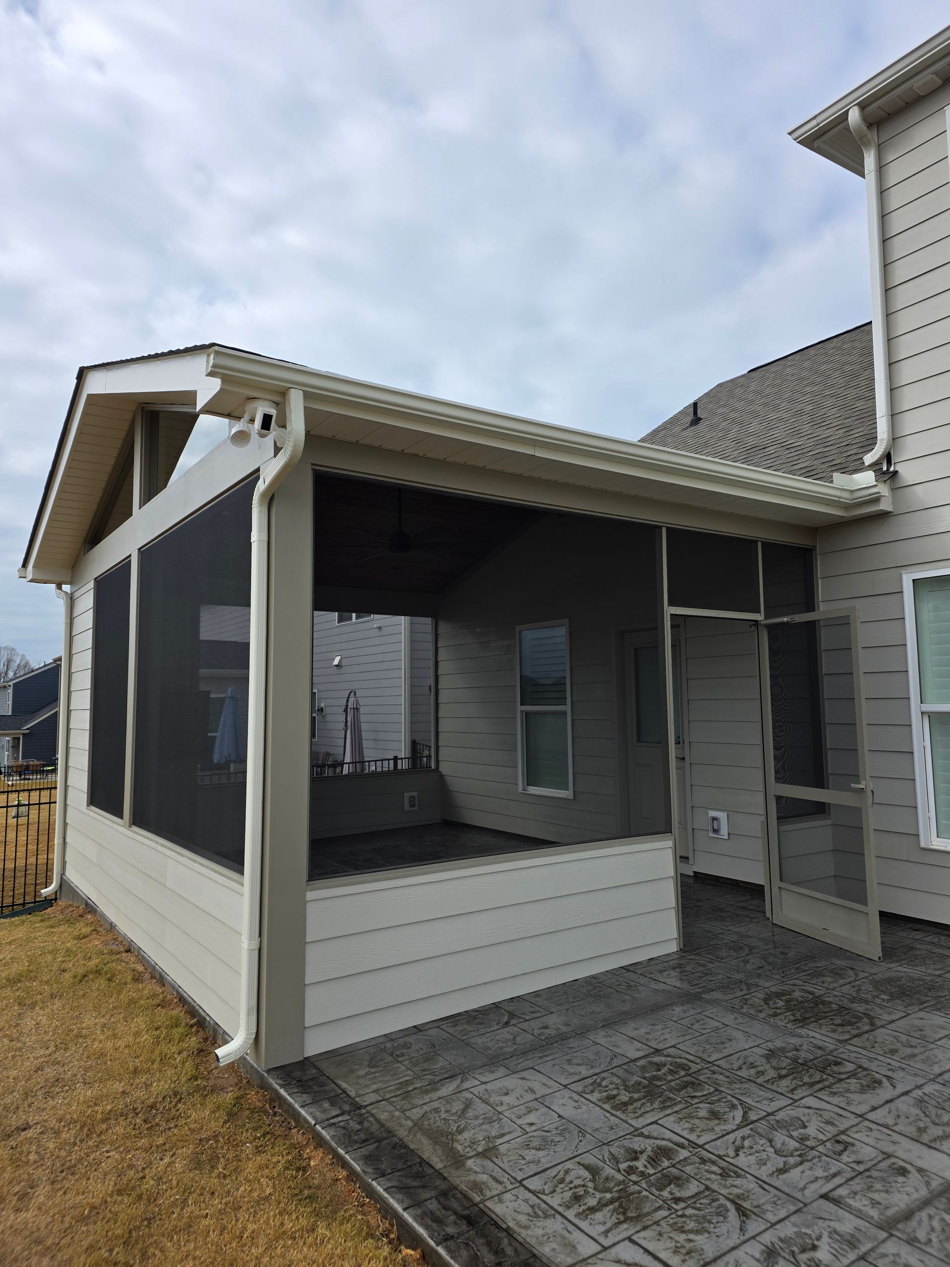 Enclosed porch with screened windows and white siding beside a stone patio under a cloudy sky