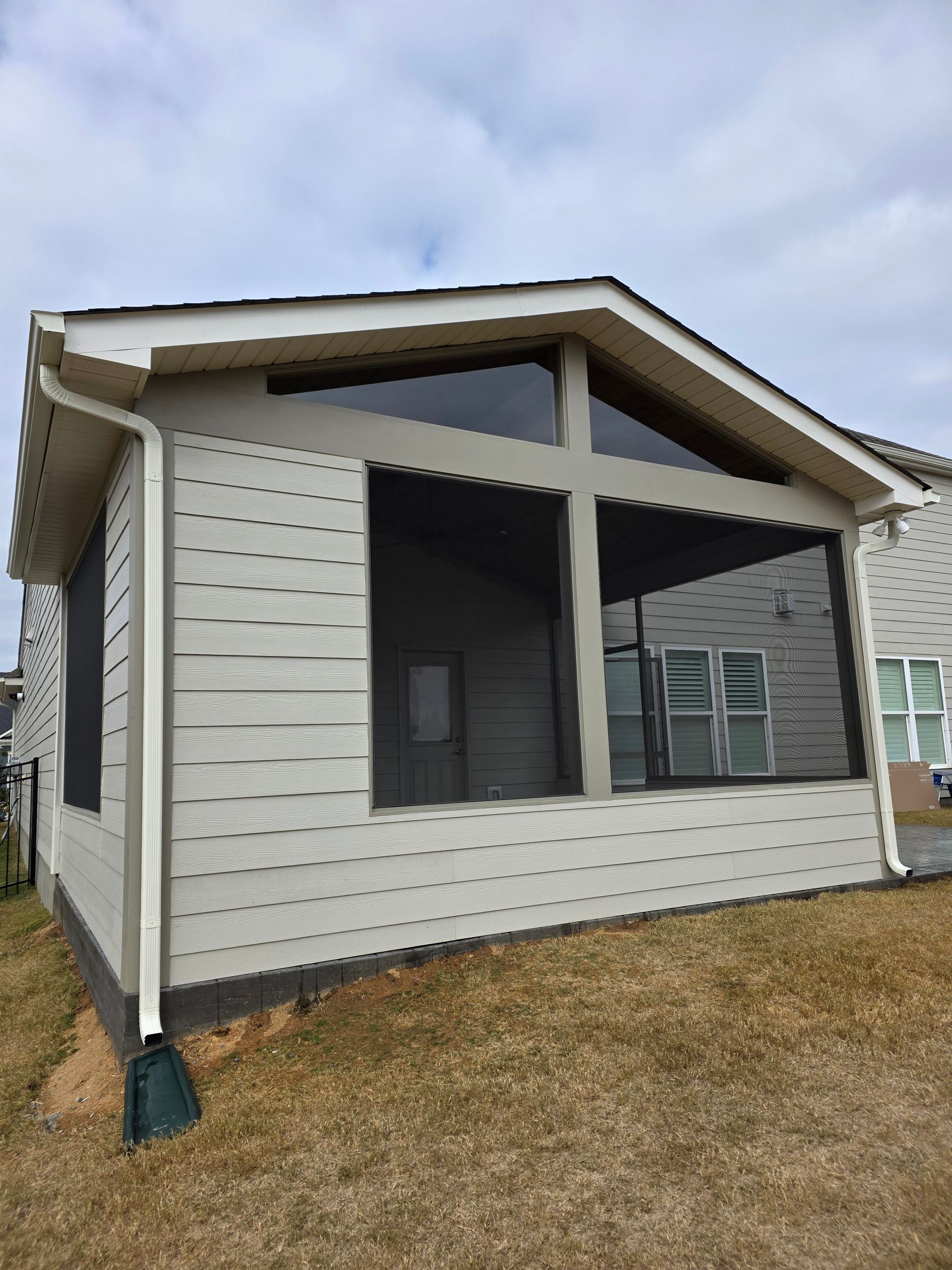 Small white house with screened porch and green shutters under a cloudy sky.