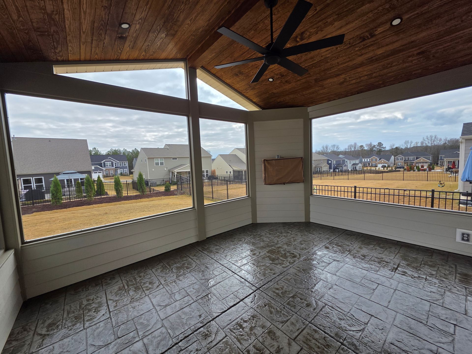 Covered porch with wood ceiling, stone floor, and open views of neighboring houses and fields.