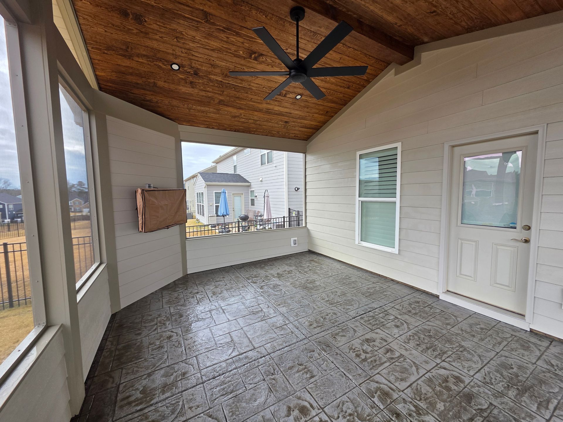 Covered porch with wood ceiling, ceiling fan, screened windows, and a door overlooking a neighborhood street.