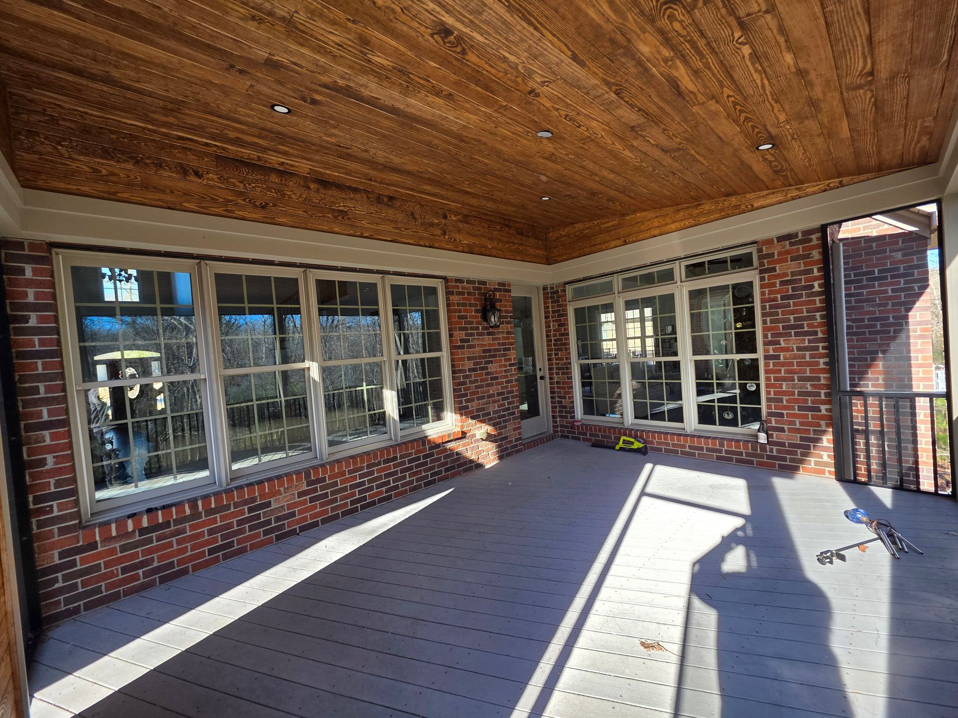 Covered brick porch with wood ceiling, large windows, and sunlight on the floor