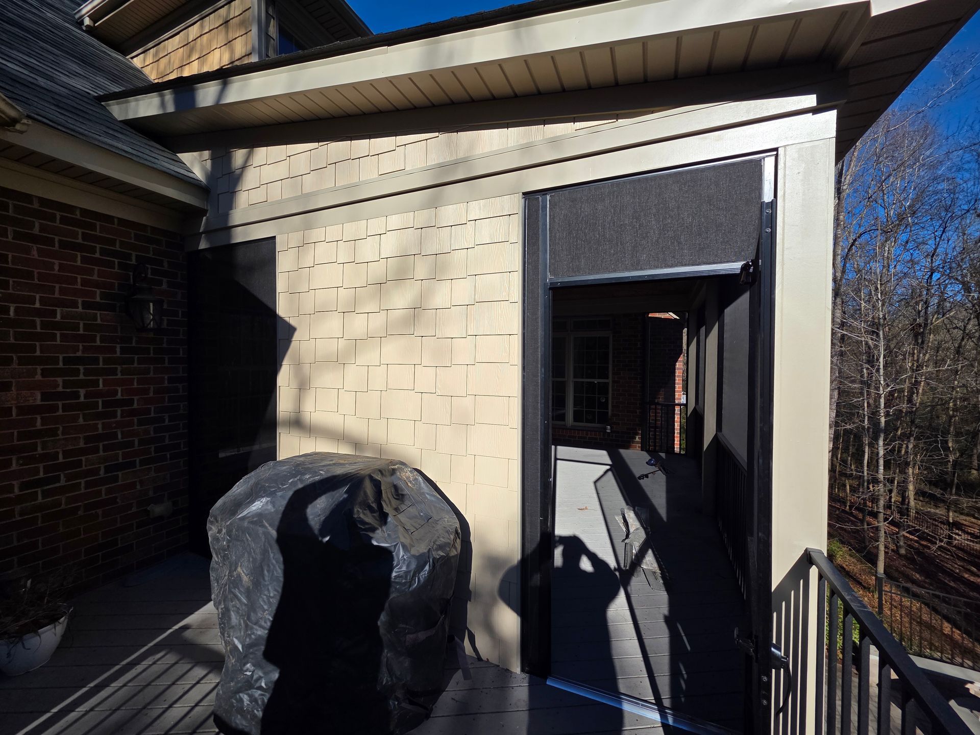 Sunlit patio with a brick wall, black tarp-covered object, and open doorway to a dim interior
