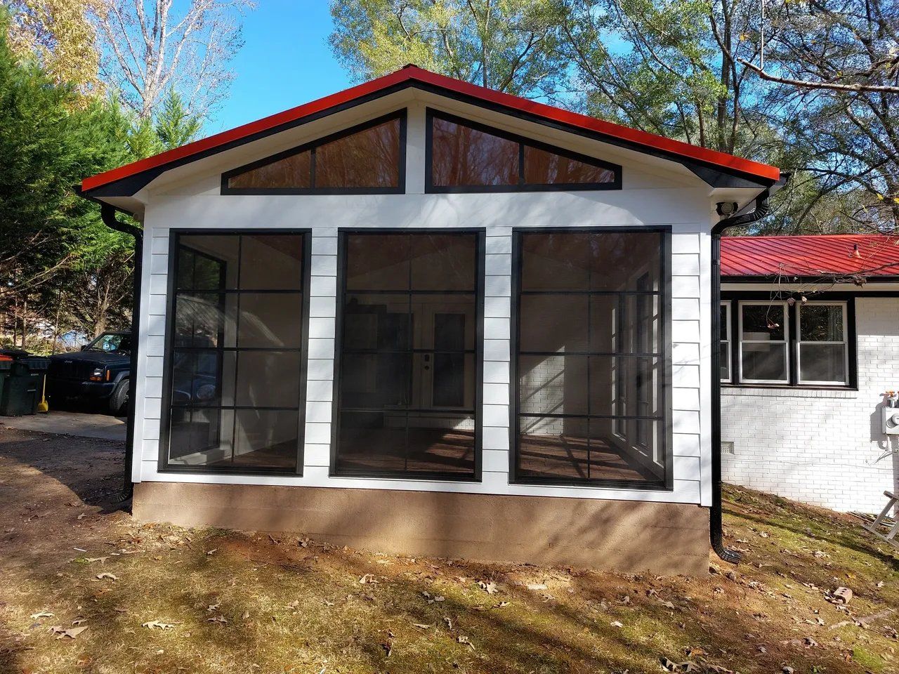 A white house with a red roof has a screened in porch