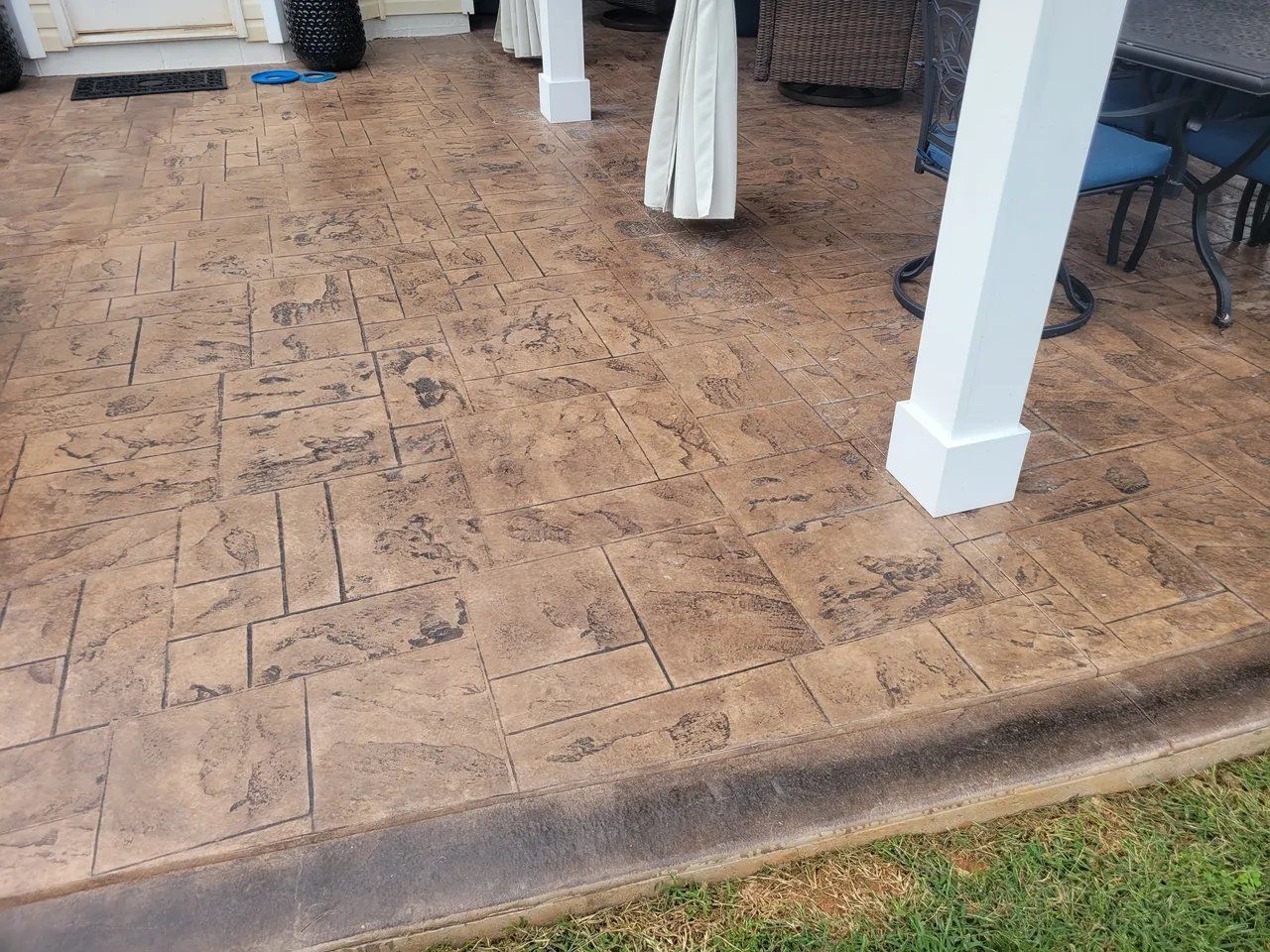Stamped concrete patio with white columns and outdoor furniture under a covered porch