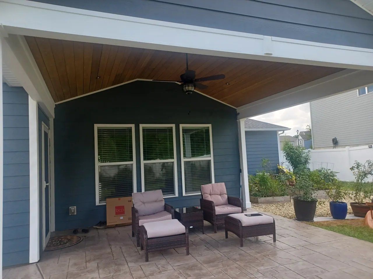 Covered patio with blue wall, white shutters, and patio chairs under a ceiling fan
