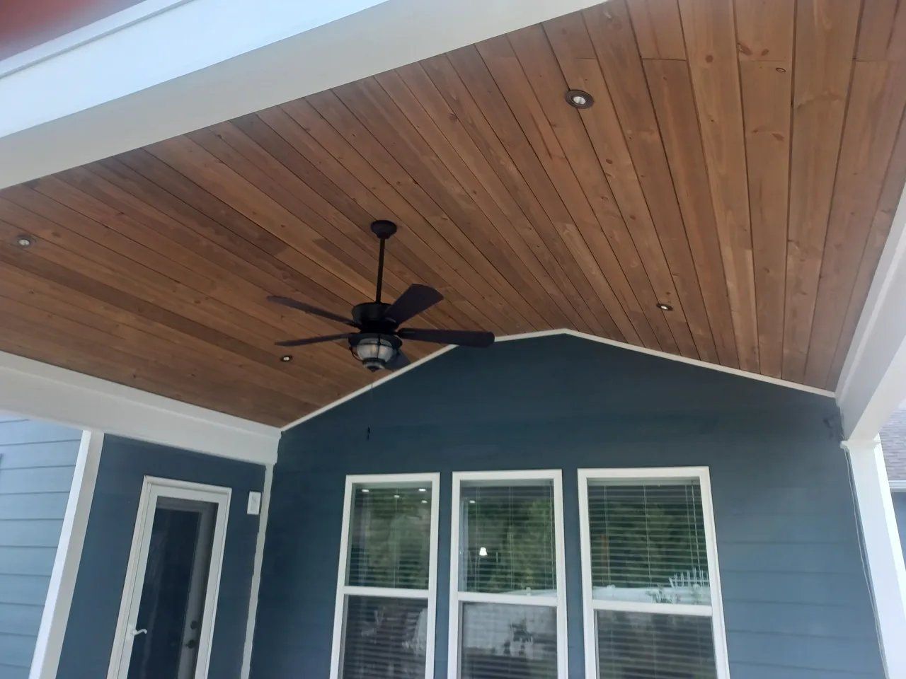 Covered porch with wood-paneled ceiling, ceiling fan, blue siding, and white-trimmed windows