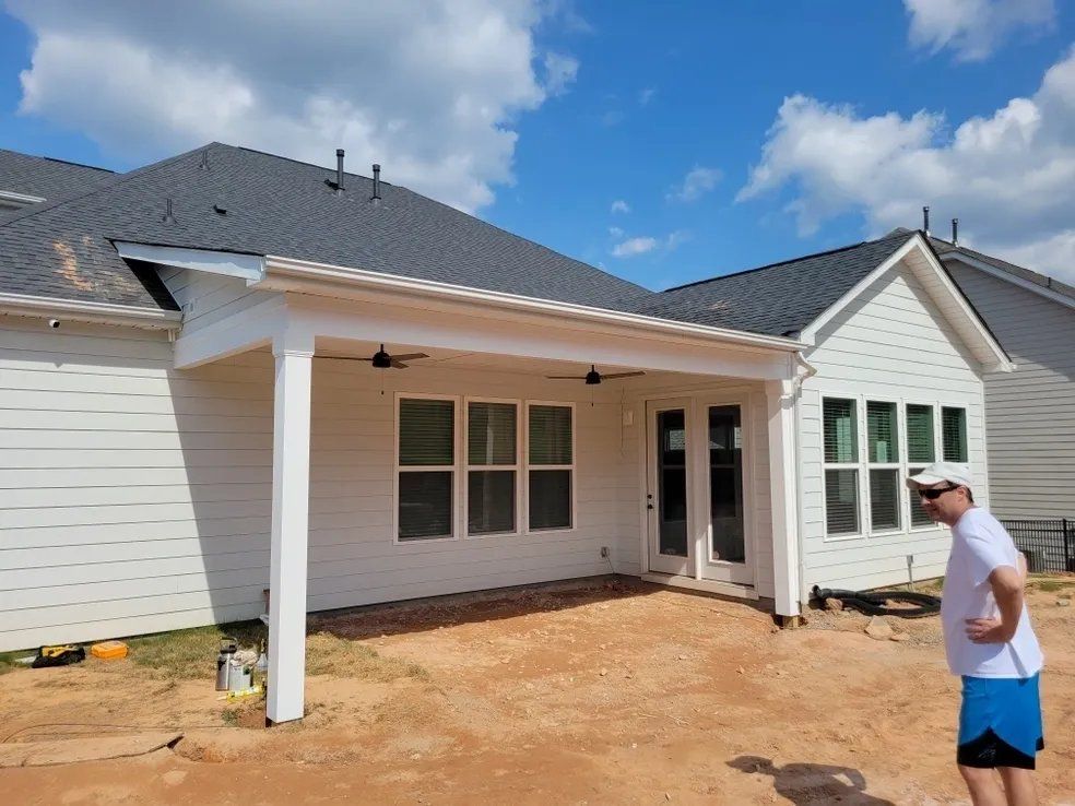 New house exterior with white siding and porch under construction; man stands in the yard