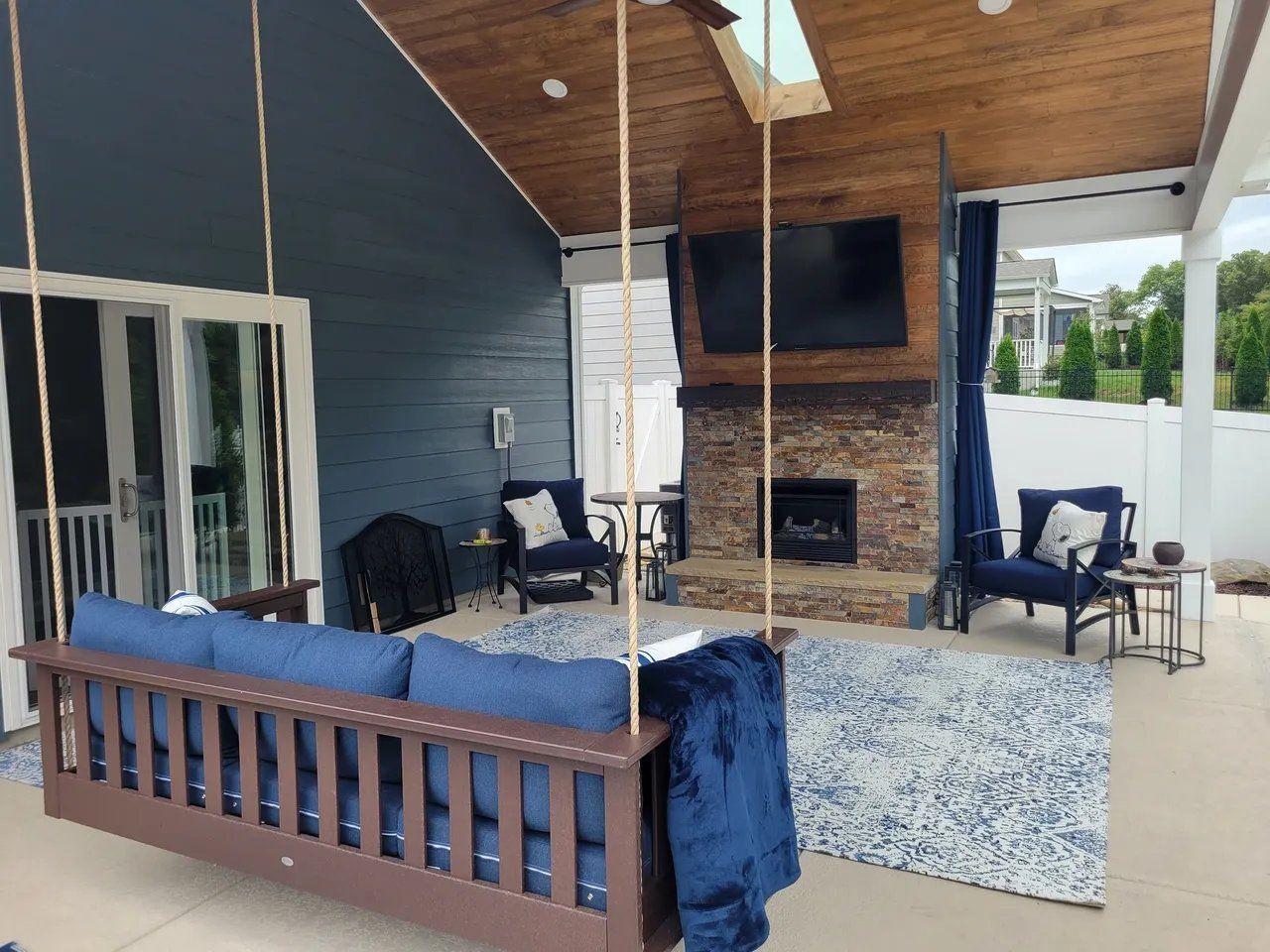 Covered patio with blue furniture, rug, TV, and stone fireplace under a wood سقف