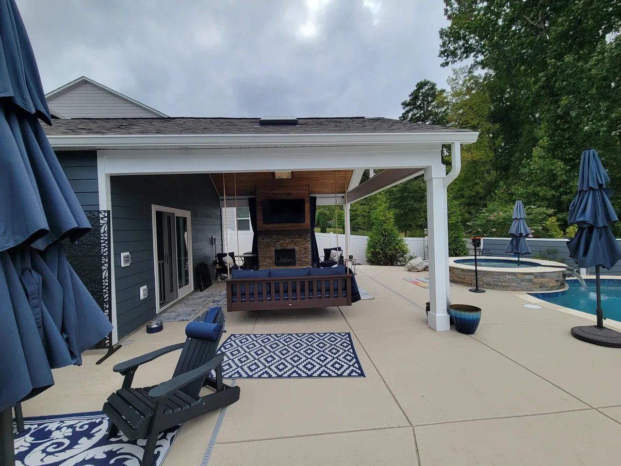 Patio with lounge chairs, blue umbrellas, dining table, and a covered outdoor kitchen by a pool