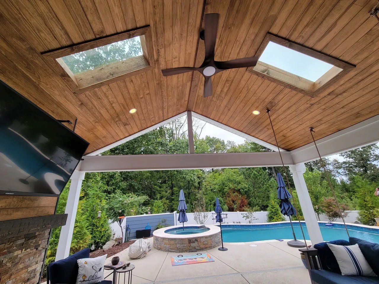 Covered patio with wood ceiling, skylights, fan, lounge seating, fire pit, and backyard pool with fountain
