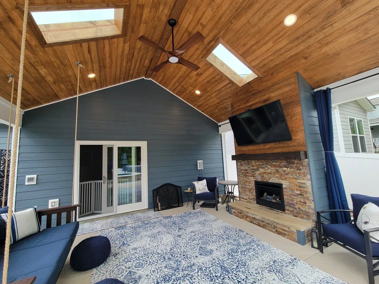 Covered patio with wood ceiling, stone fireplace, blue siding, and sliding glass doors